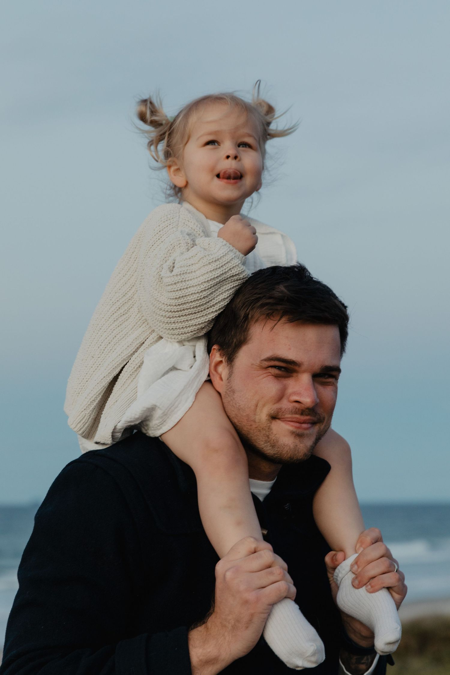 A joyful moment captured at the beach with playful shoulder rides against a blue sky backdrop.
