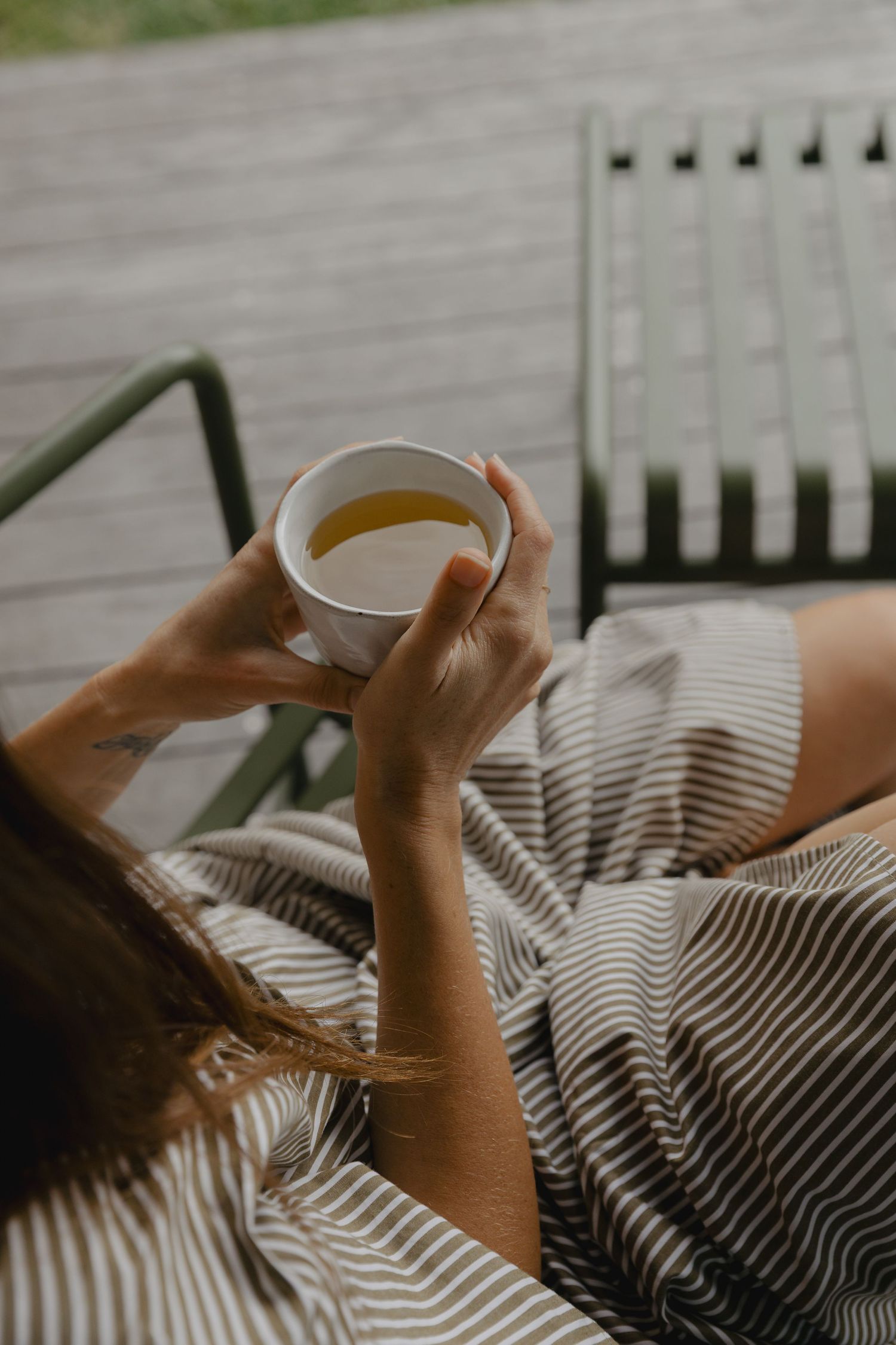 Hands holding a cup of tea while relaxing on a striped blanket.