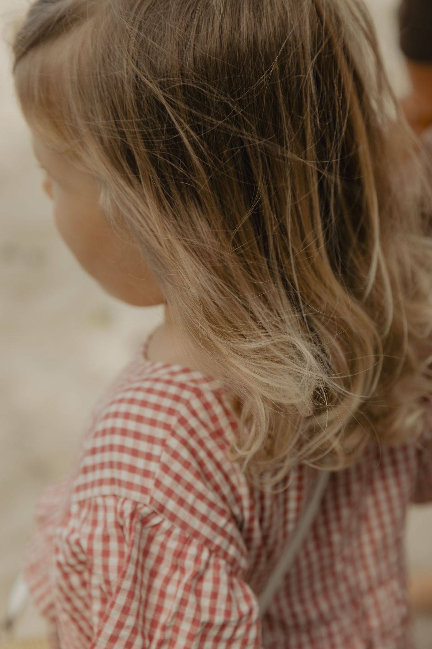 Close-up view of blonde hair and red gingham dress pattern.