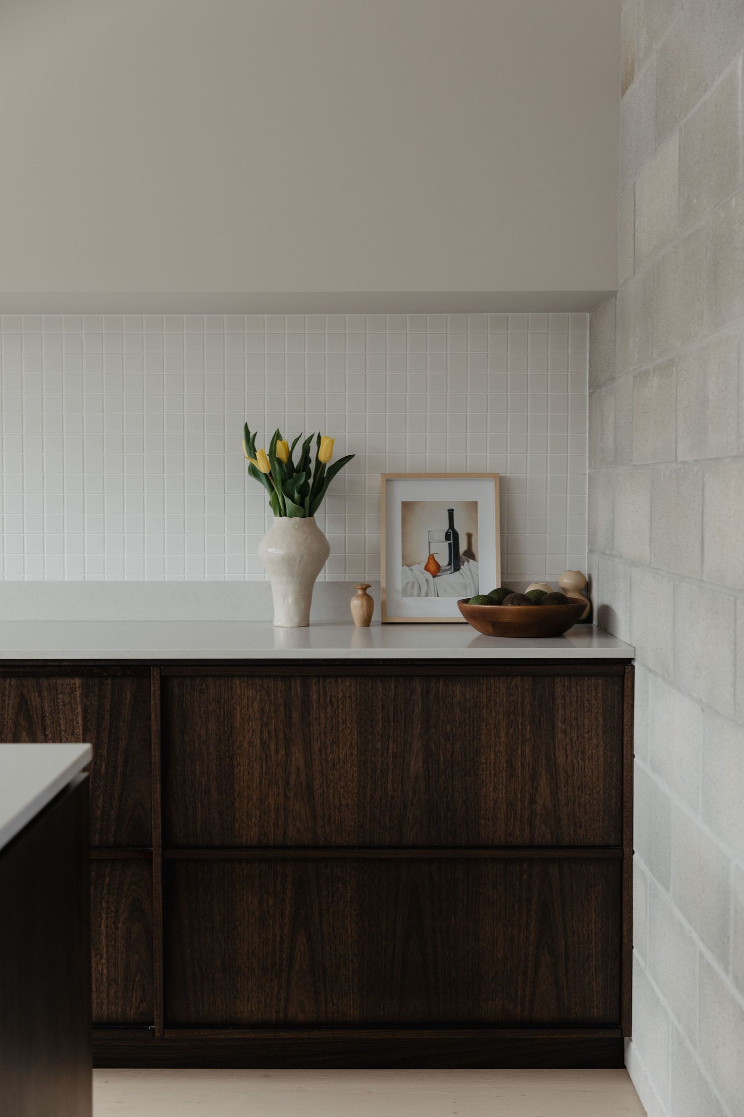 Modern kitchen corner with dark wood cabinets, white walls, and yellow tulips in a vase.