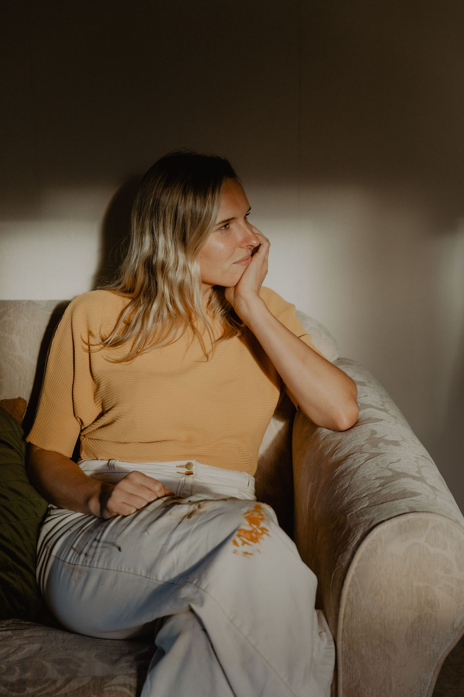 Person in yellow shirt relaxing on beige couch in moody lighting.