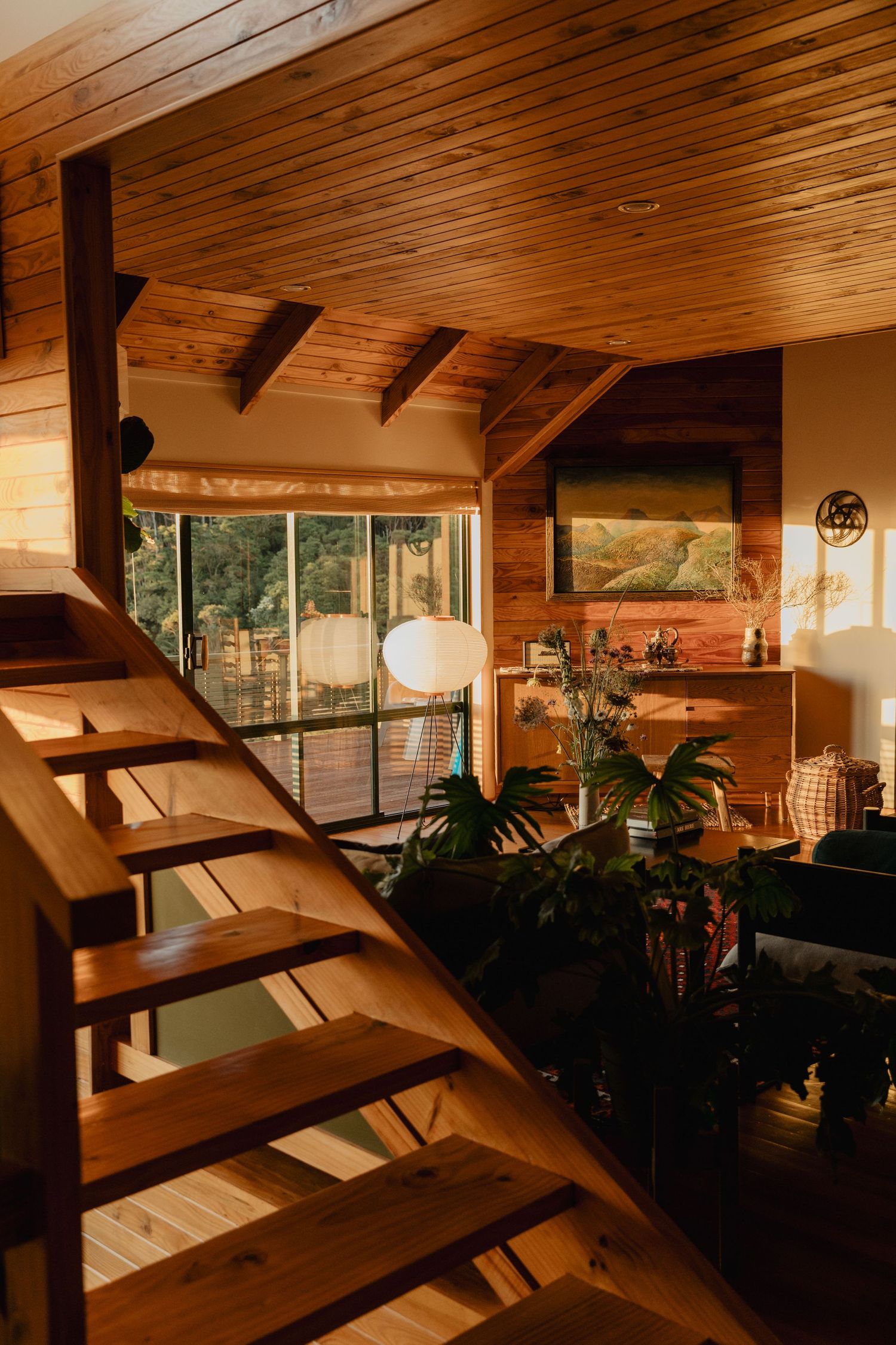 Modern wooden interior with slanted ceiling and large windows featuring indoor plants.