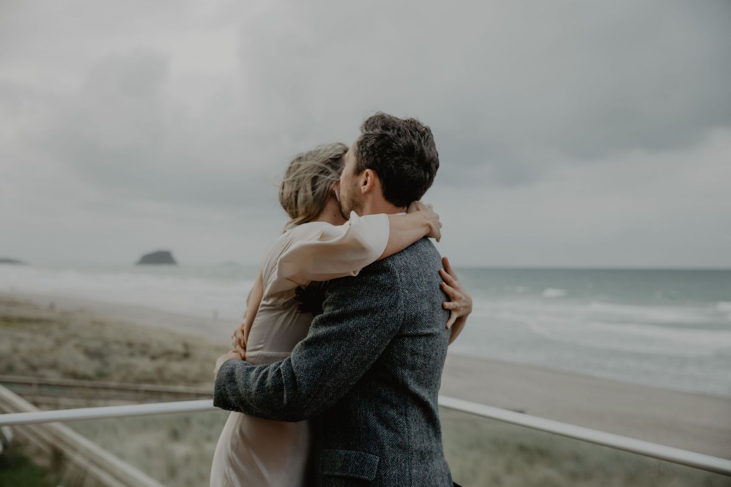 Couple embracing on a cloudy beach with waves in the background.