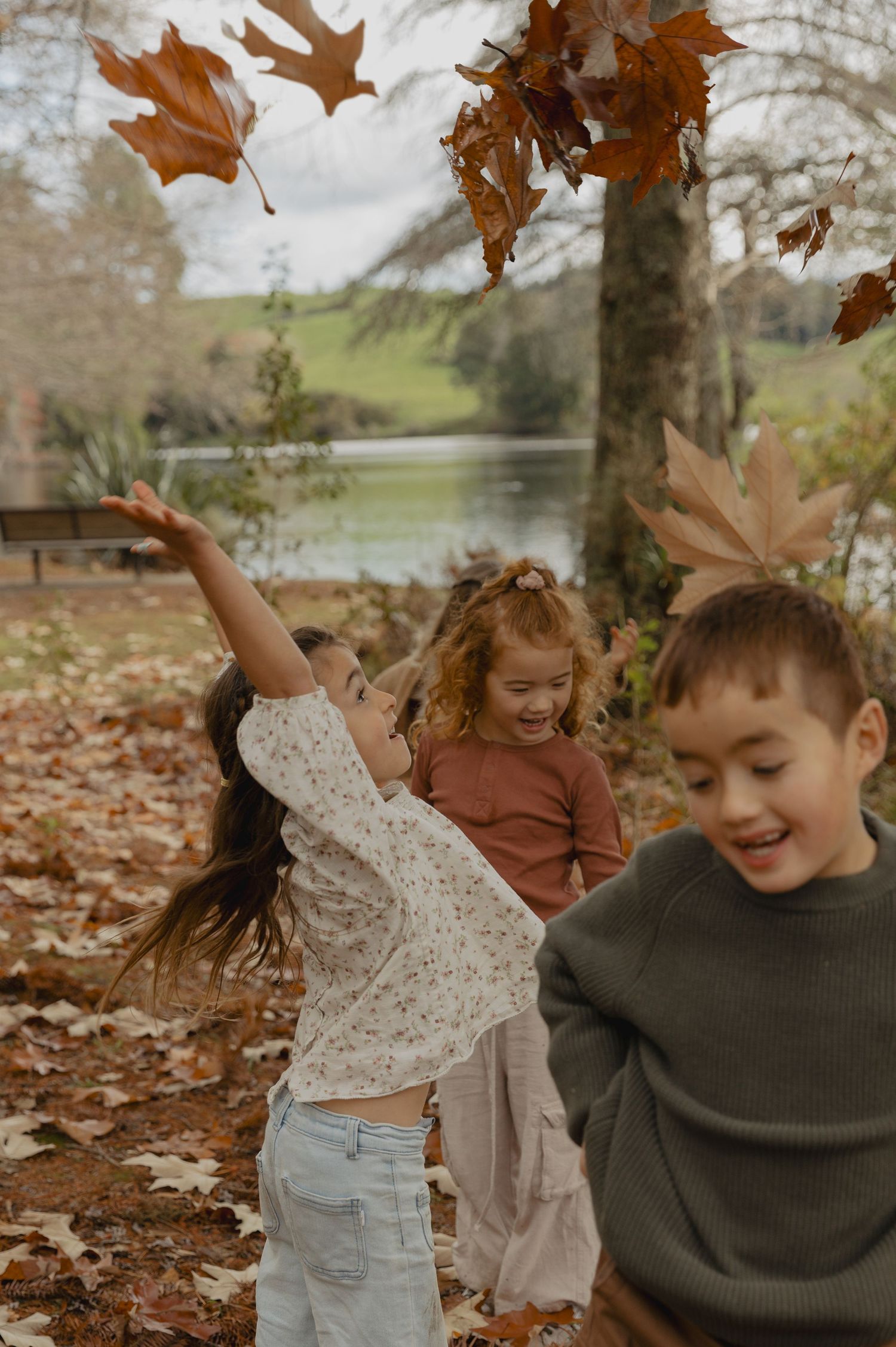 Children playing with autumn leaves in a park on a fall day.