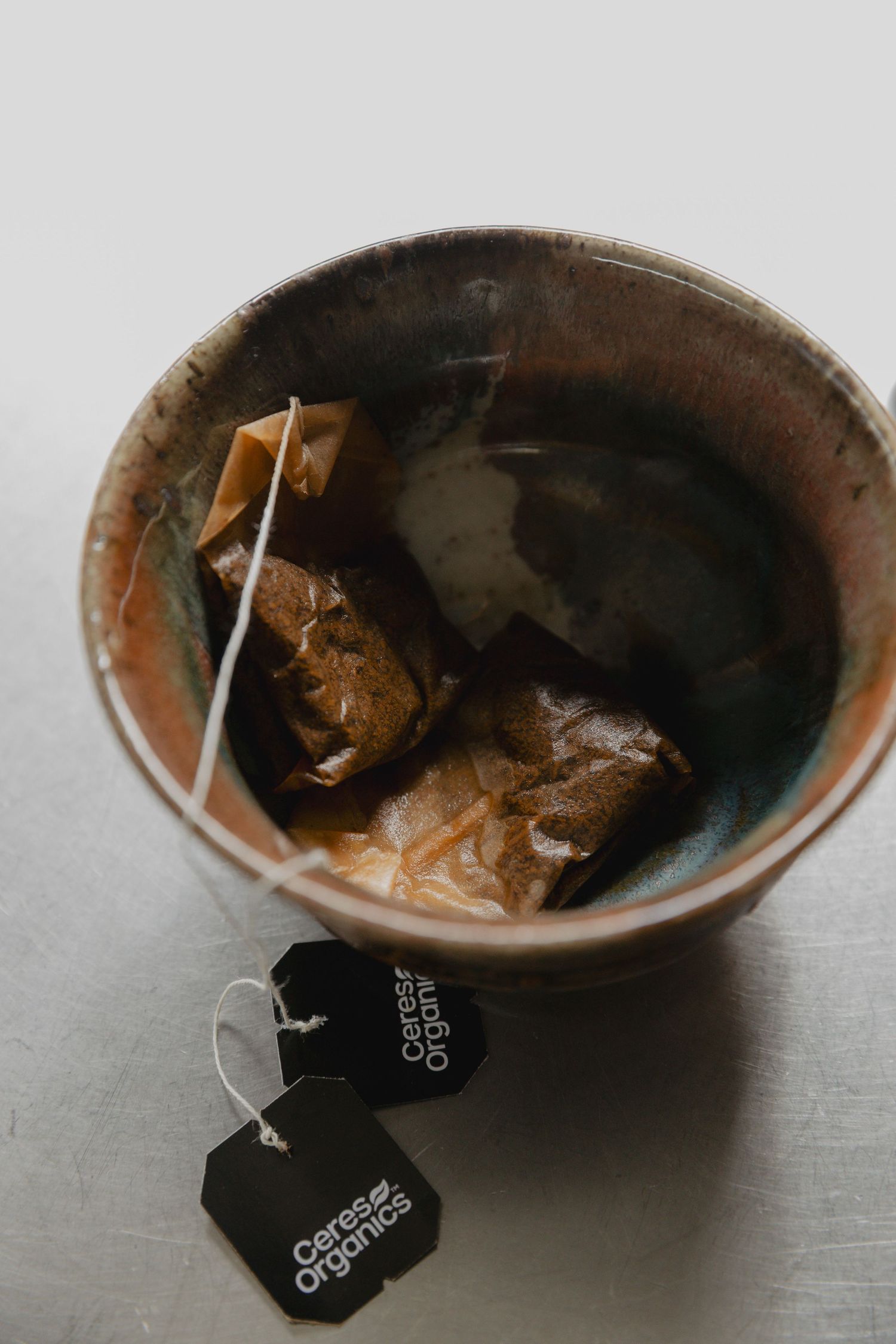 Used tea bags steeping in a dark ceramic cup with brand tags visible.