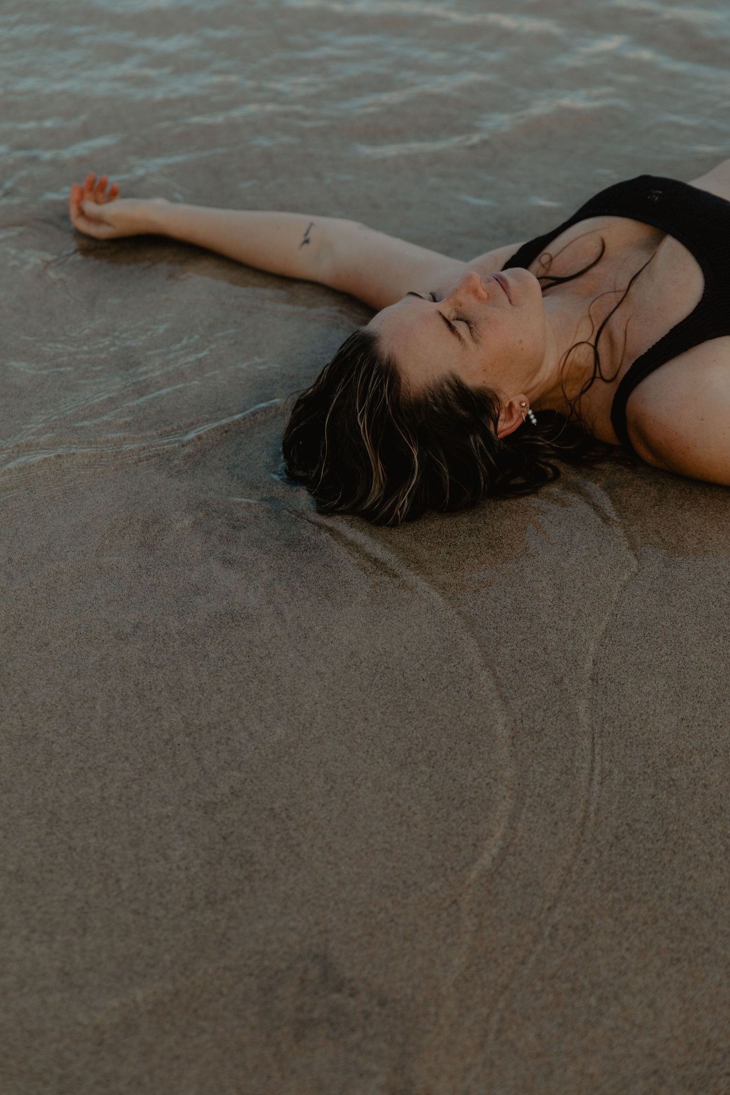 A person lies peacefully on wet sand as waves wash up on the beach.