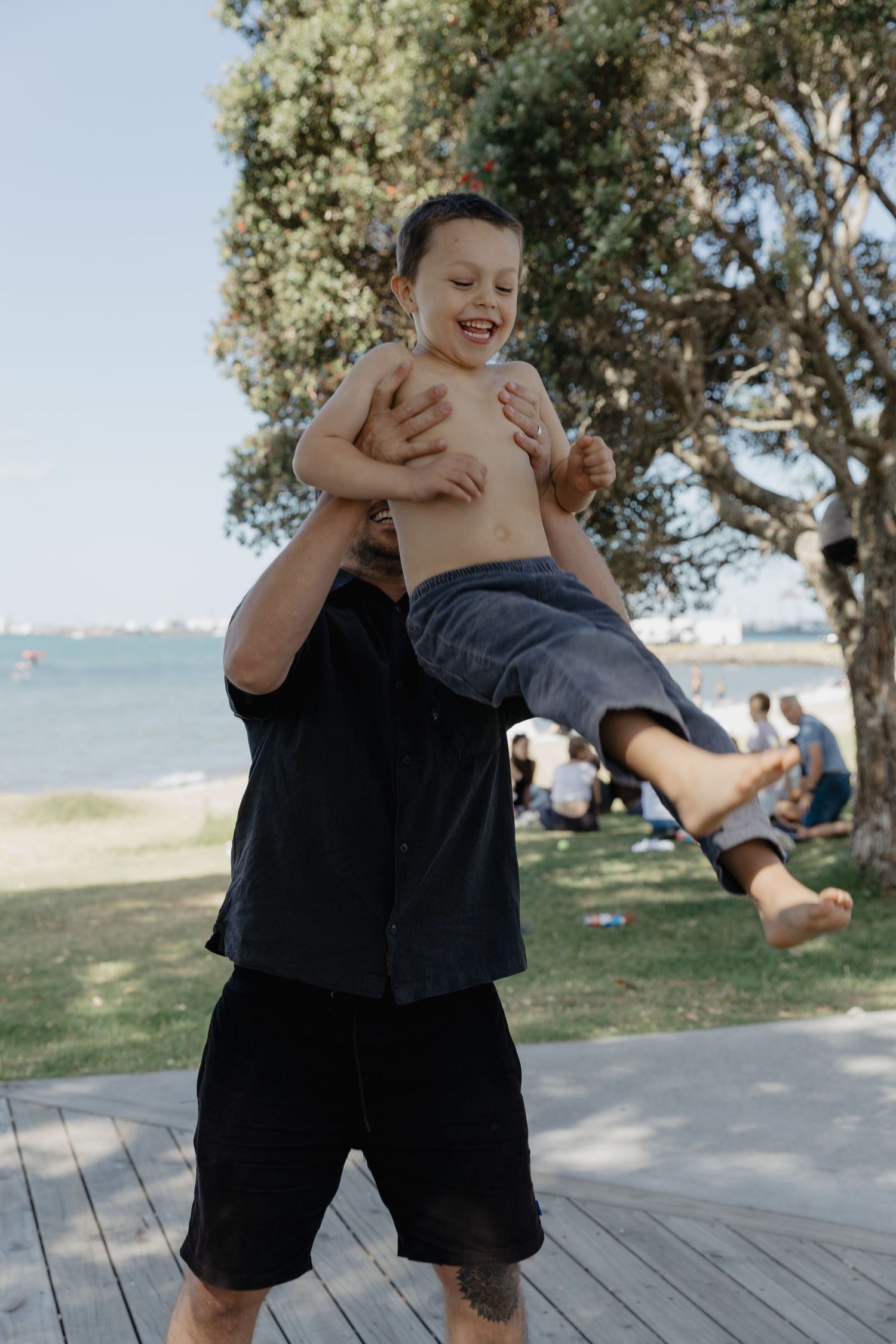 Child playing and jumping on wooden boardwalk near beach with trees in background.