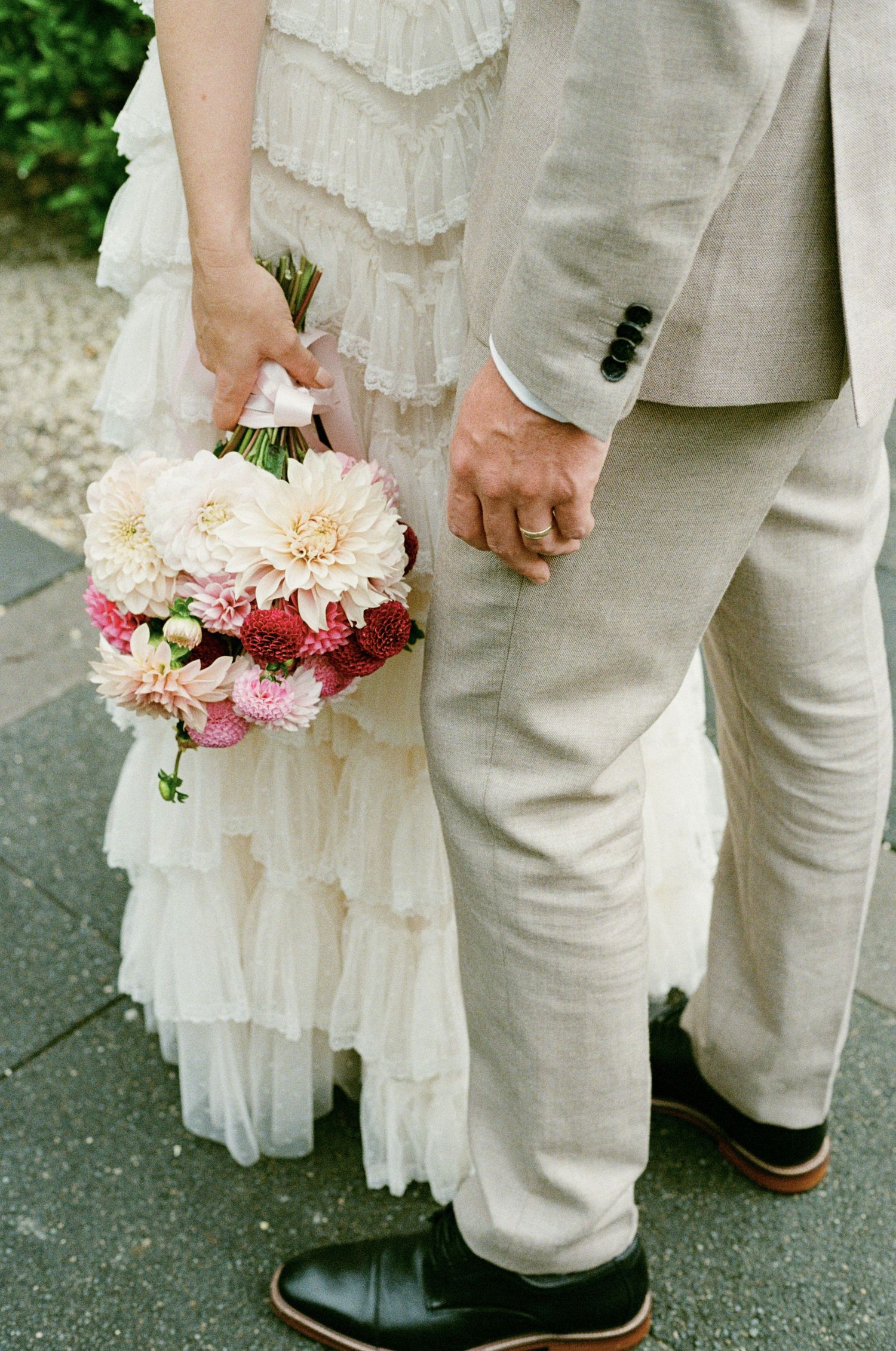 Pink and peach floral bouquet held against white dress and light gray suit.