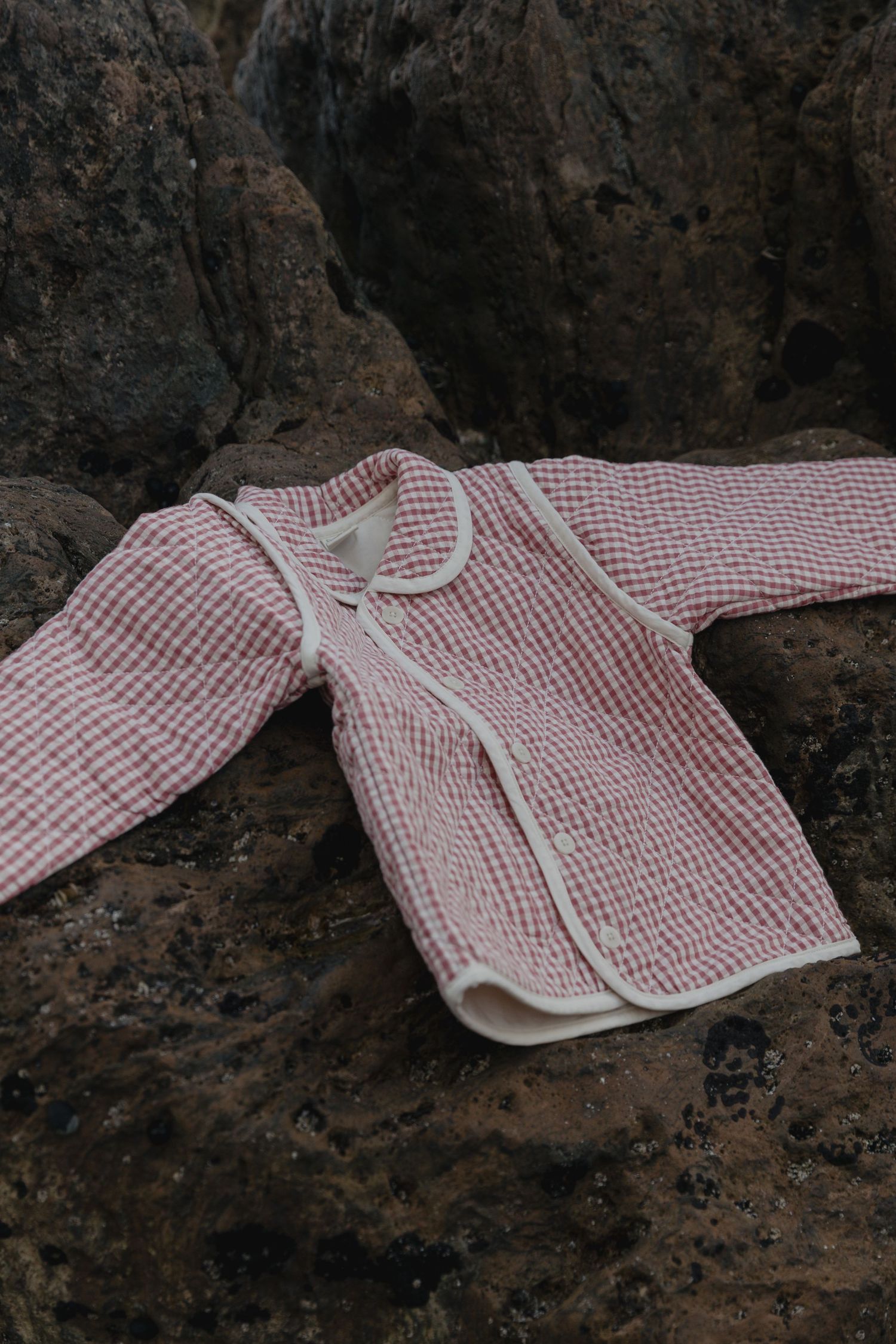 A red and white checkered garment laid out on dark rocky surface.