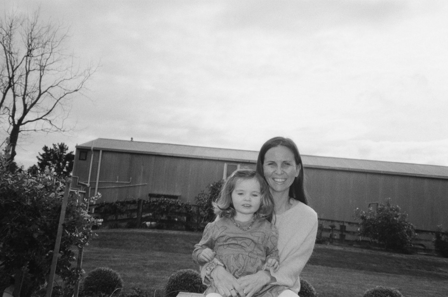 Black and white portrait of mother and child outside industrial building.