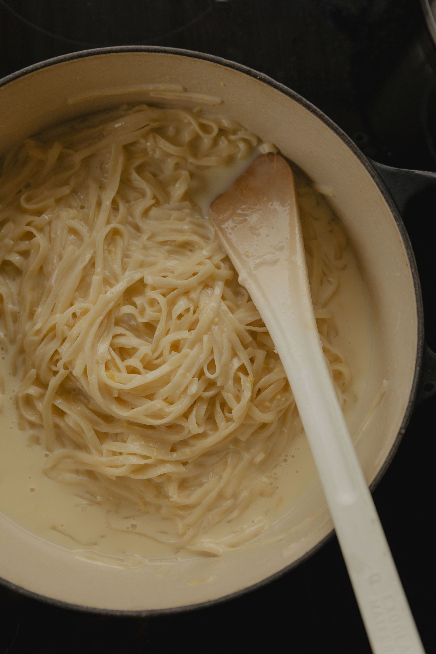 Fresh cooked noodles in a white ceramic pot with wooden spoon.
