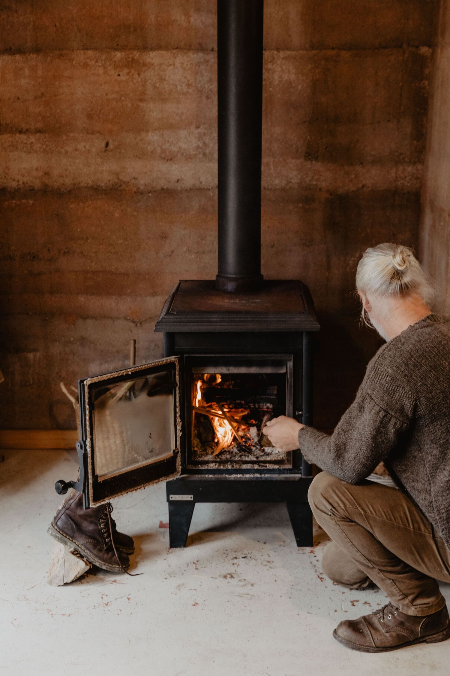 Person tending to wood burning stove in rustic interior setting.