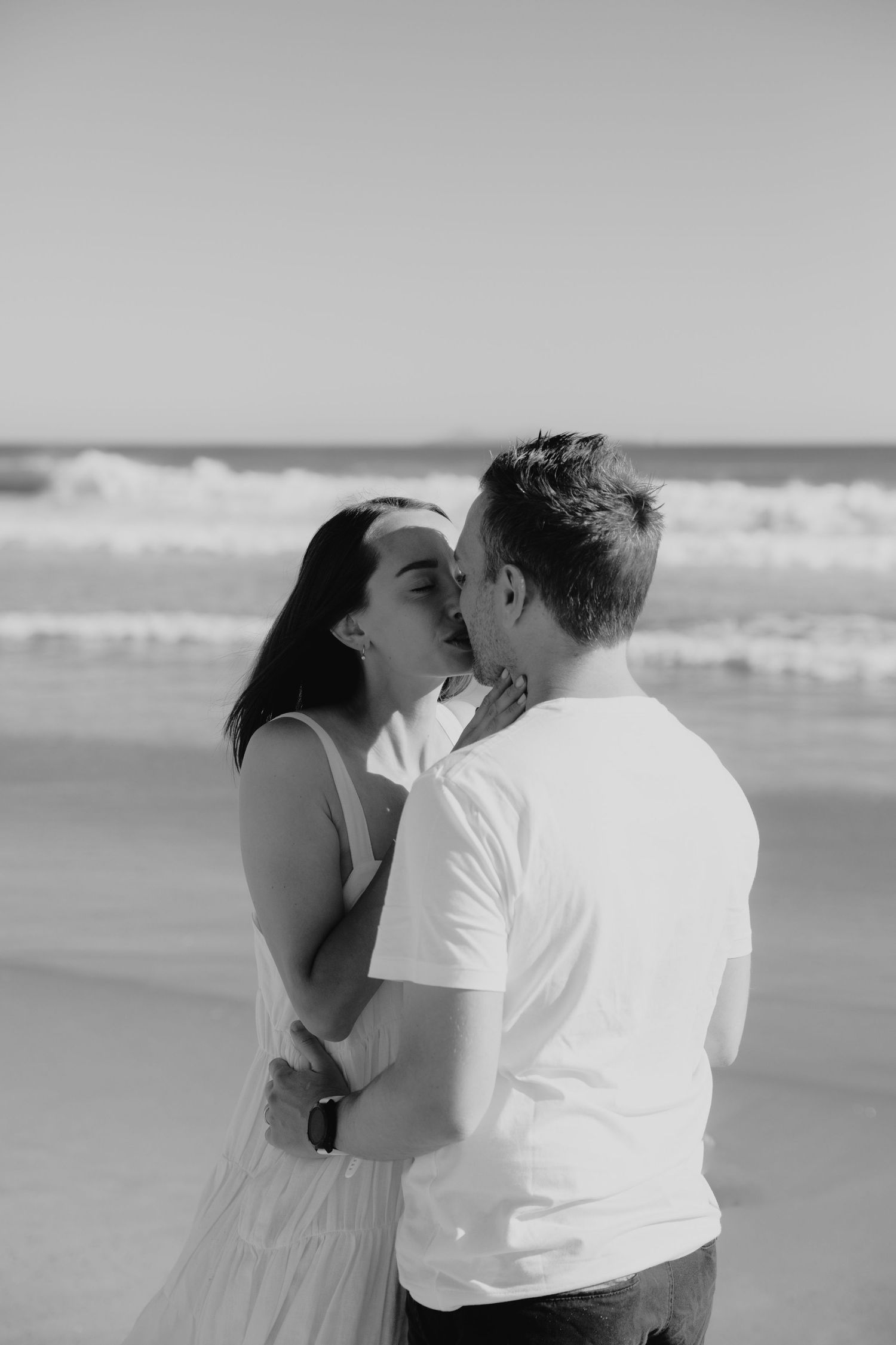 Intimate black and white beach portrait with waves crashing in background.