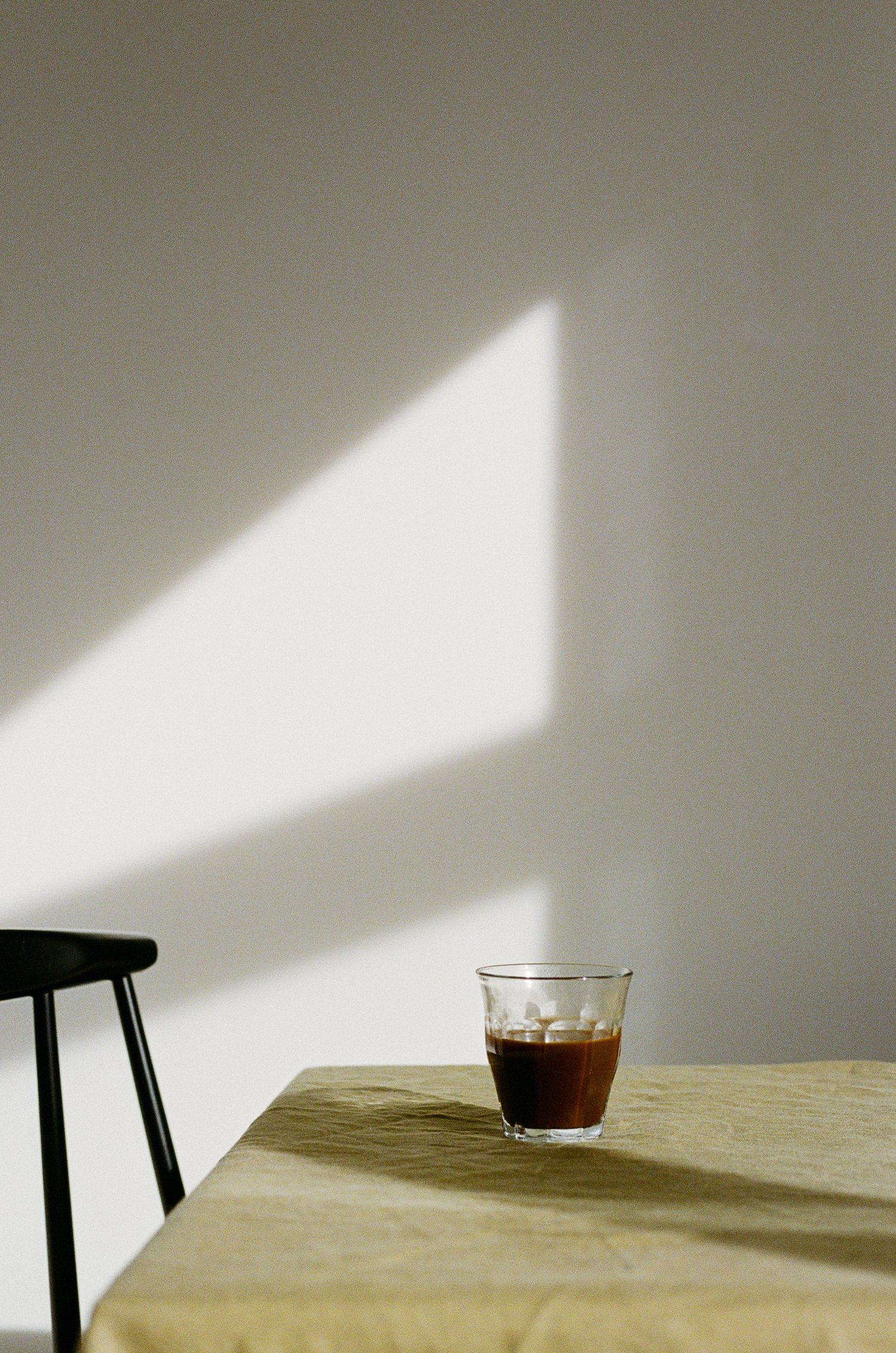 A cup of dark coffee sits on a wooden table casting dramatic shadows against a white wall.