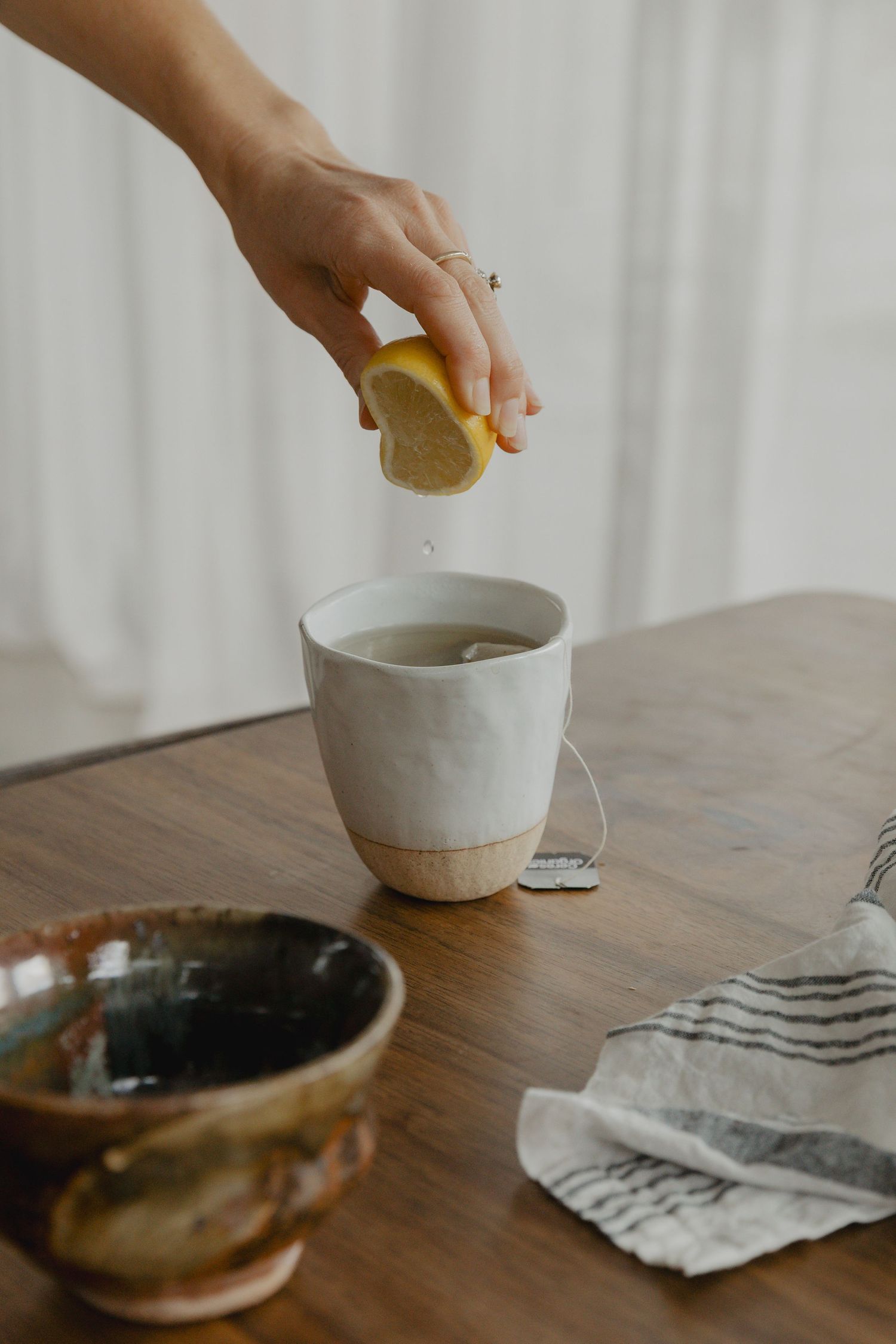 Someone squeezing lemon into a cup of tea on a wooden table with striped napkin.