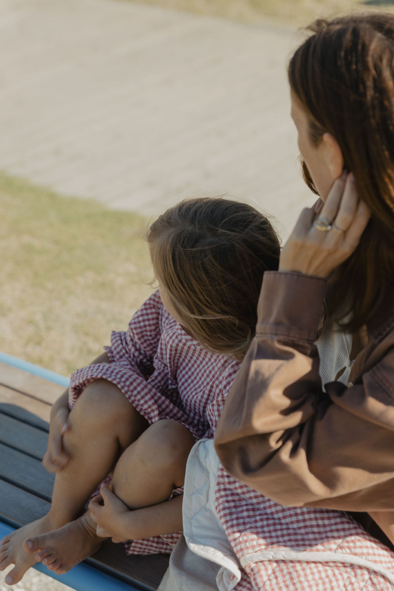 Children sitting together on a bench in matching gingham dresses.