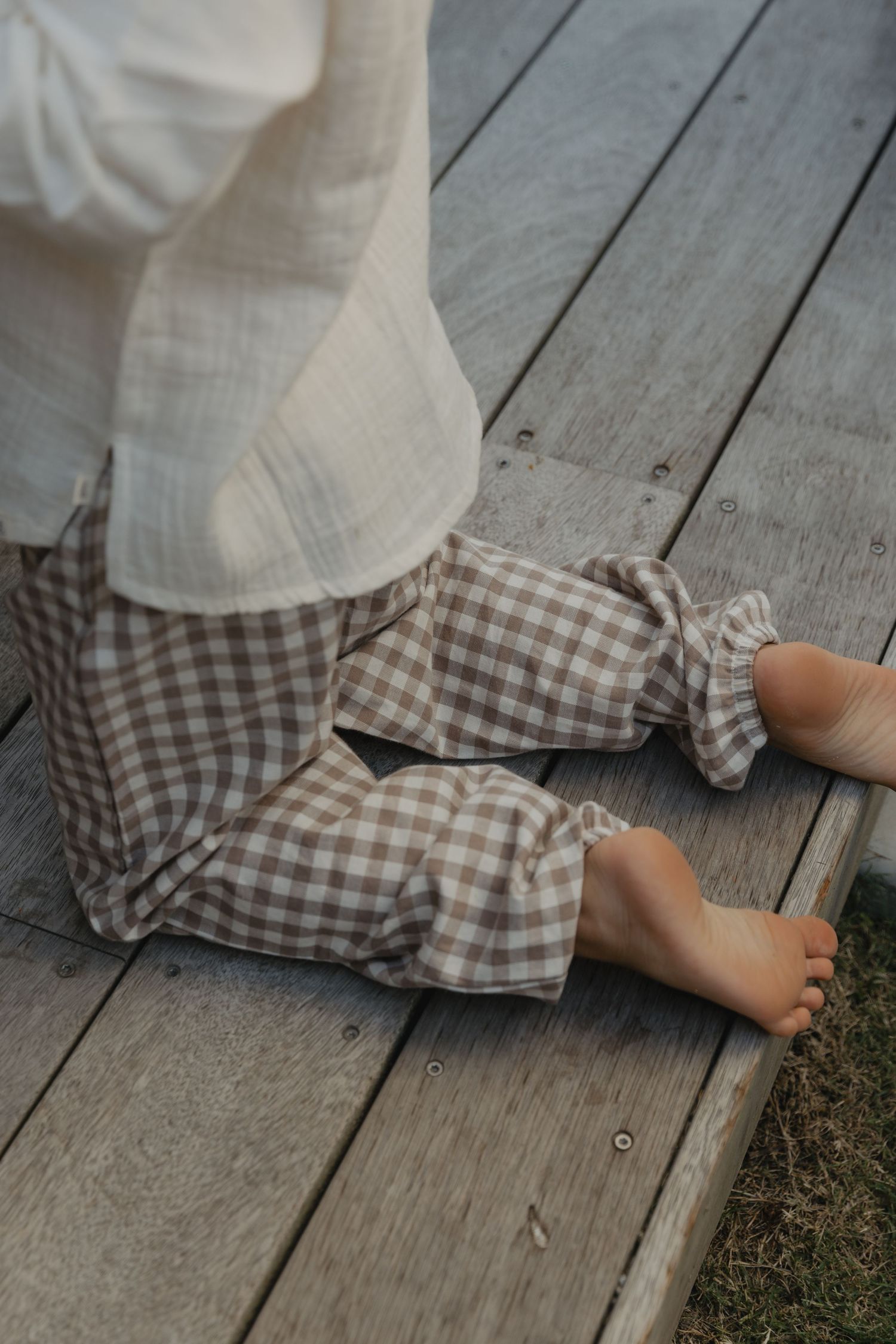 Bare feet in gingham clothing resting on wooden deck boards.