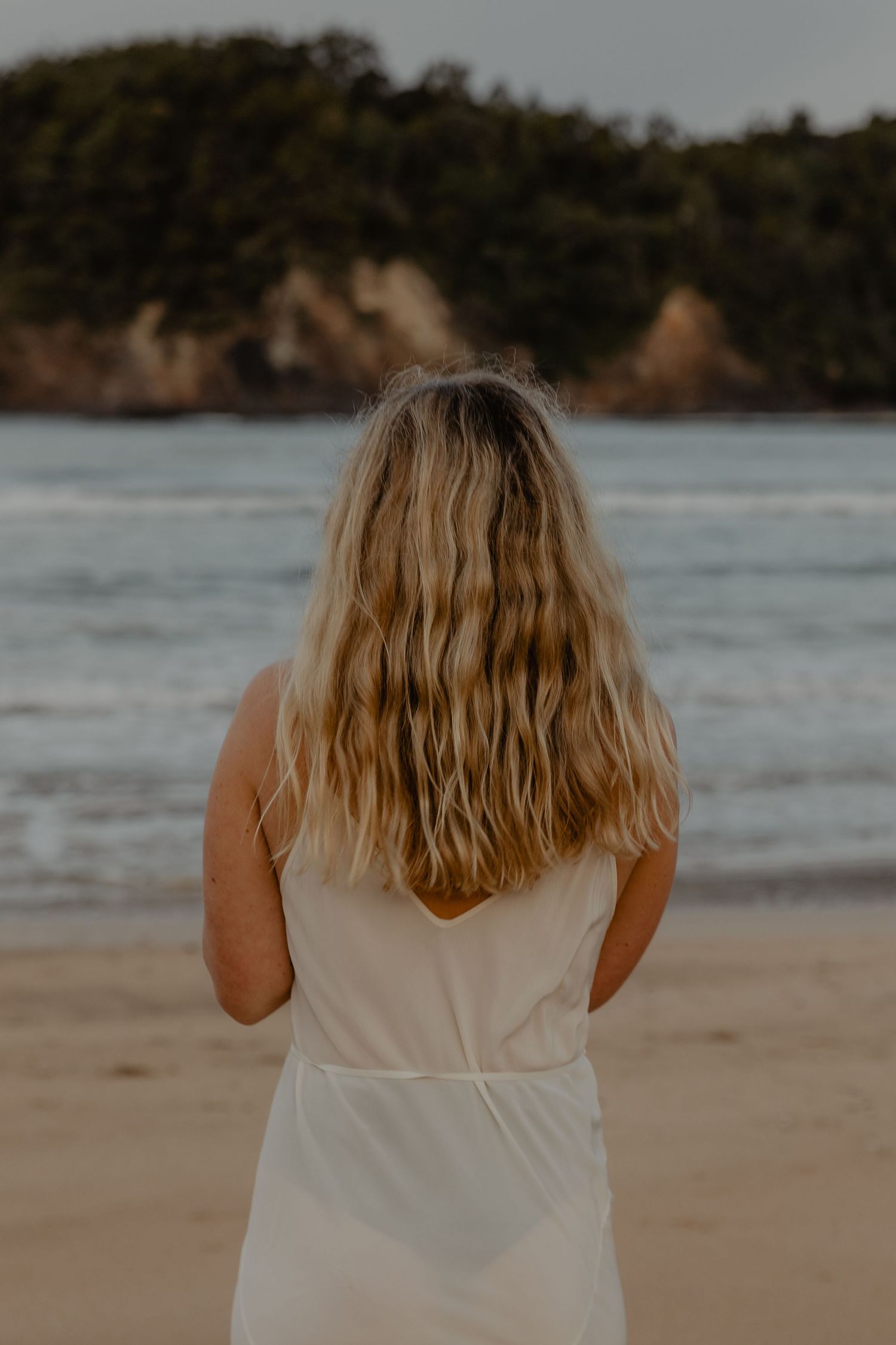 A beachside view from behind showing long blonde hair against an ocean backdrop.