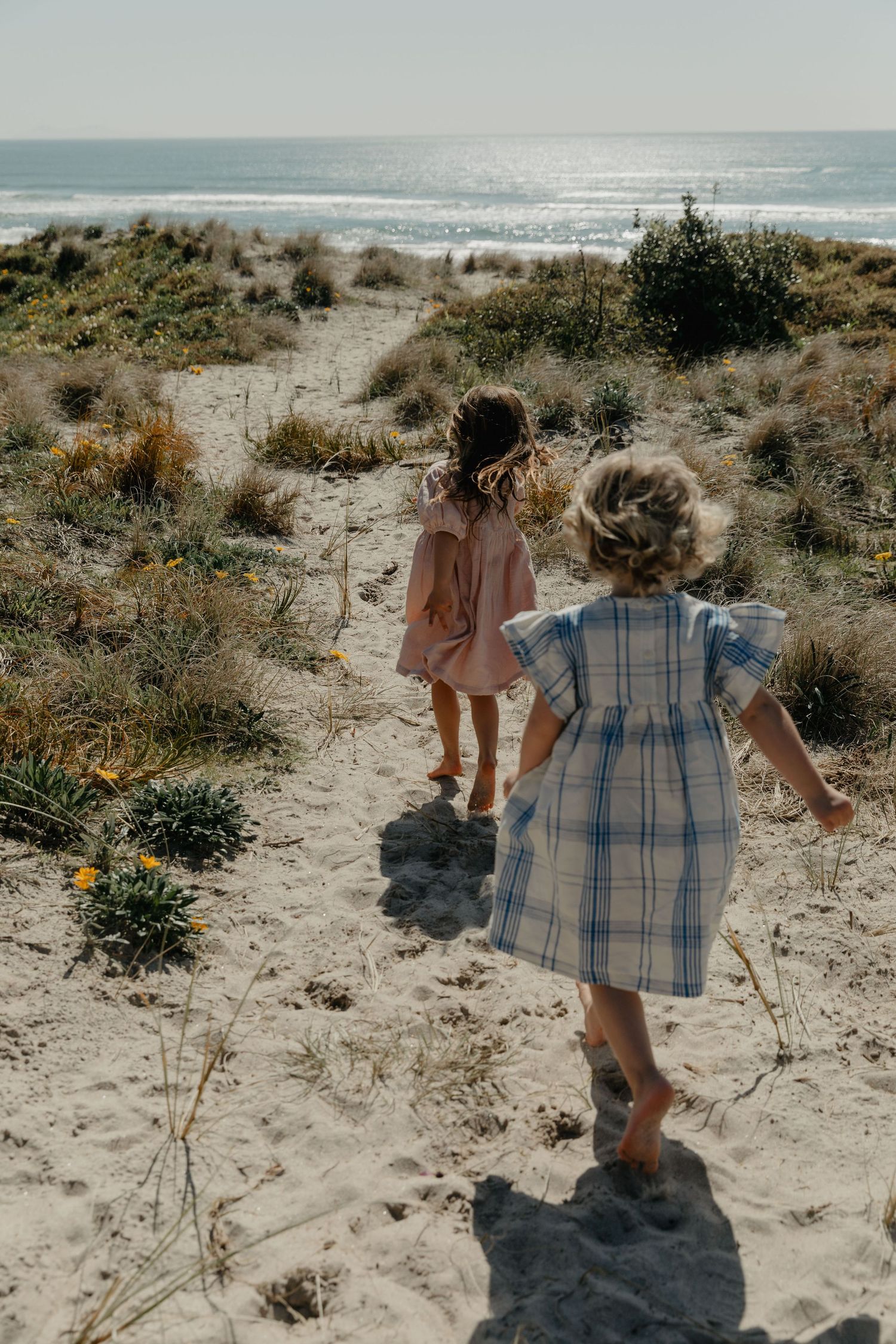 Children walking through sandy dunes near the ocean on a bright sunny day.