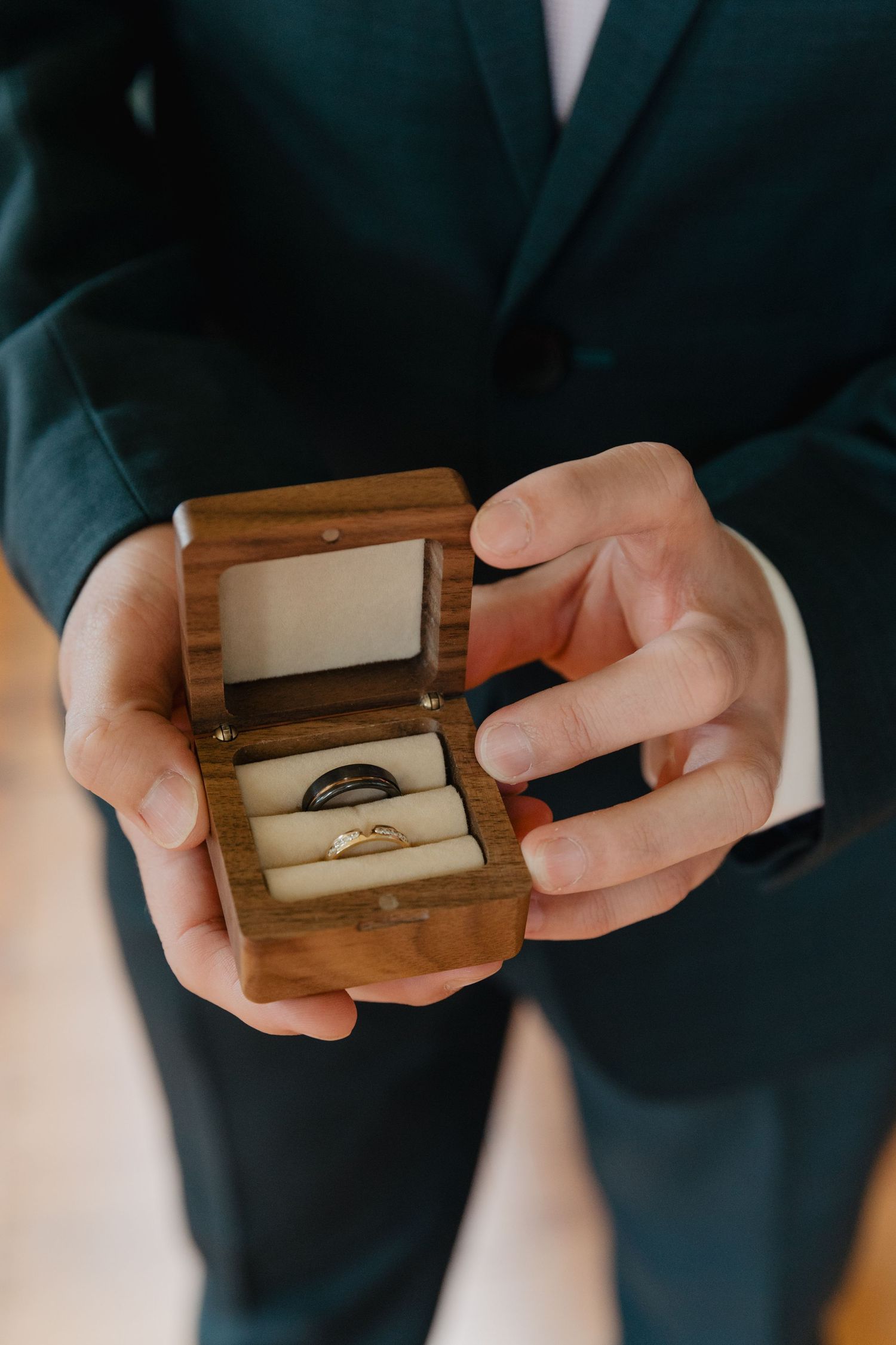 Close-up of hands holding a wooden ring box with wedding bands inside.