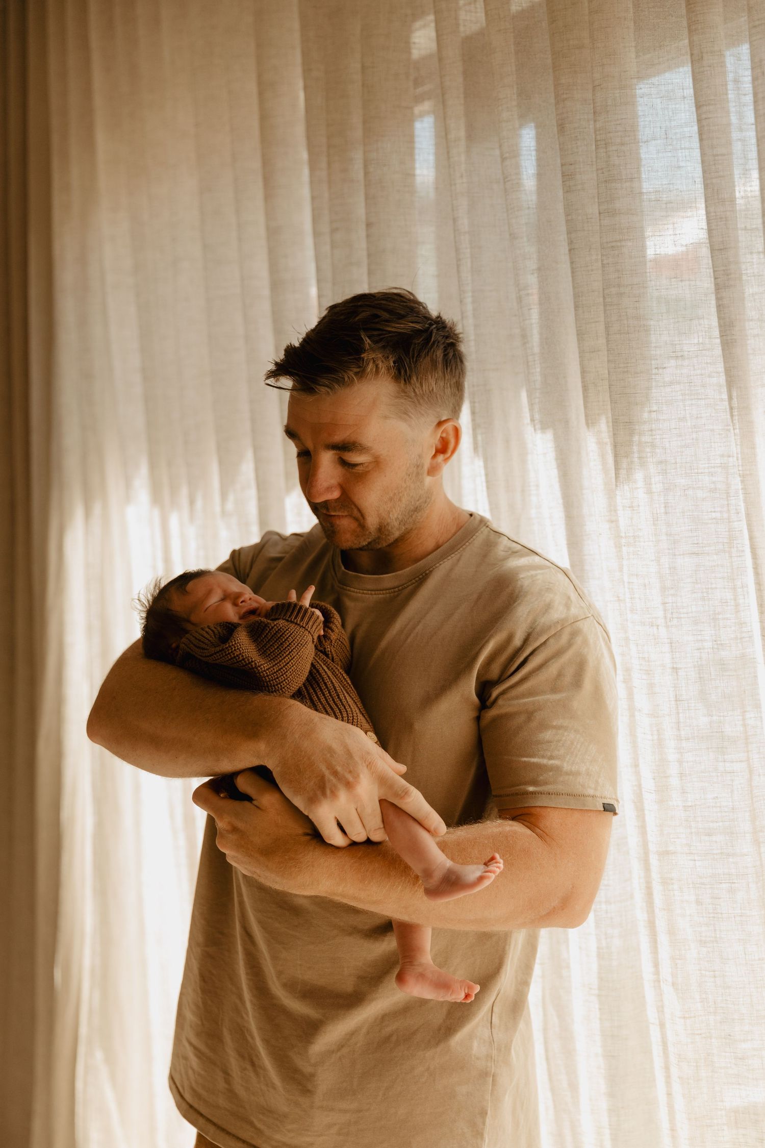 Parent holding and comforting small child in sunlit room.