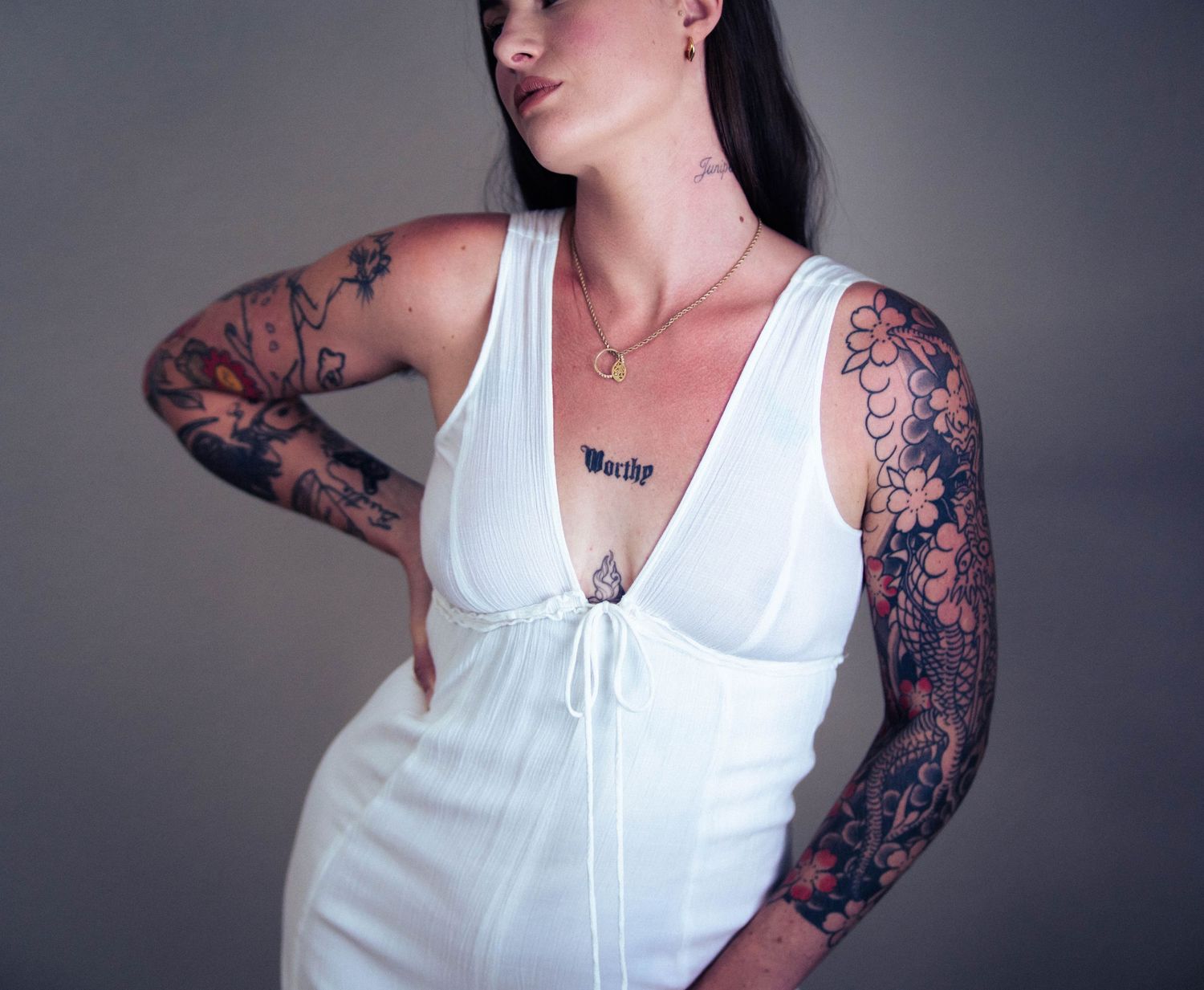 Woman in white tank top displaying detailed floral sleeve tattoo artwork.