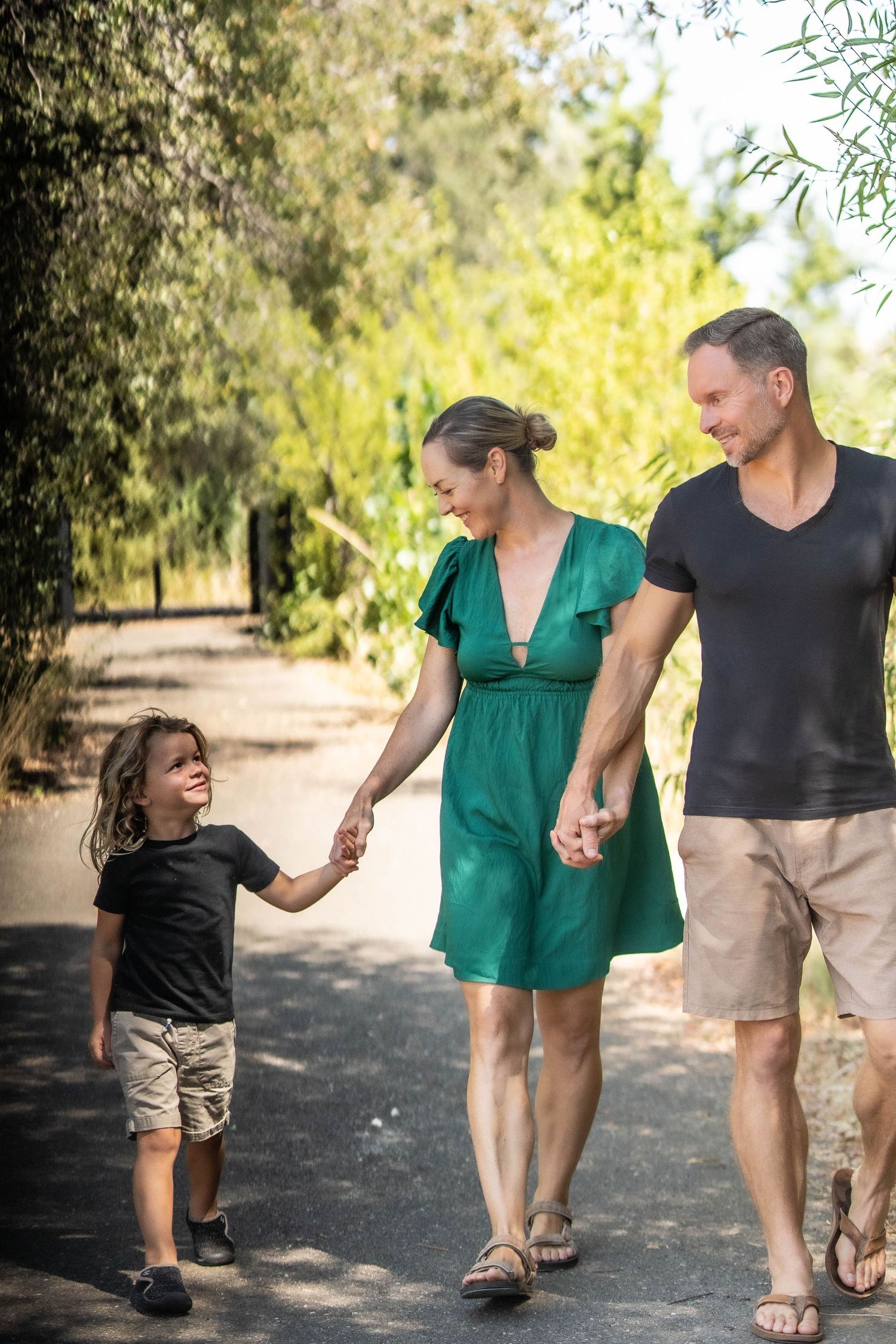 Family walking together on tree-lined path holding hands in summer.
