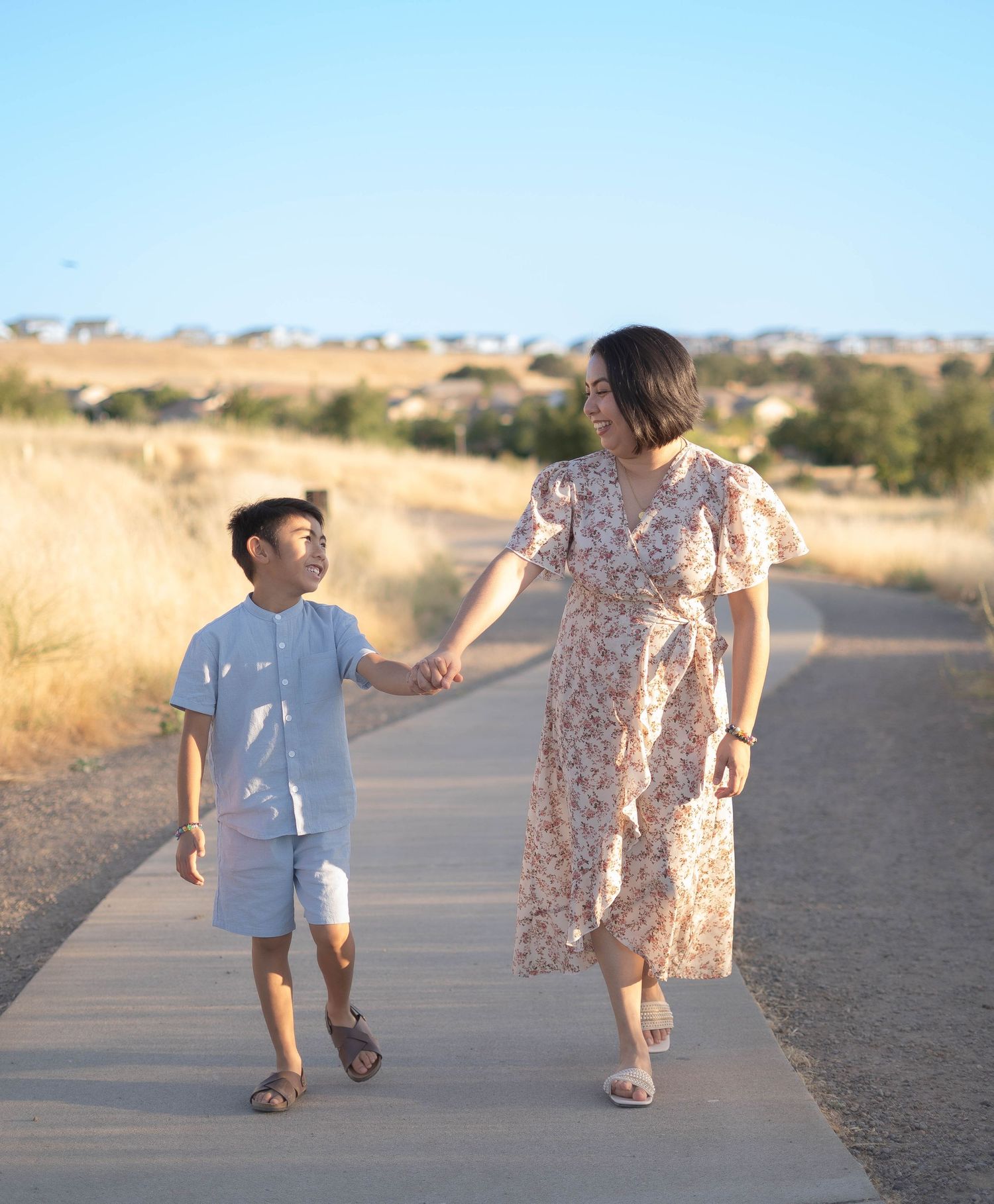 A parent and child walk hand in hand along a desert path at sunset.