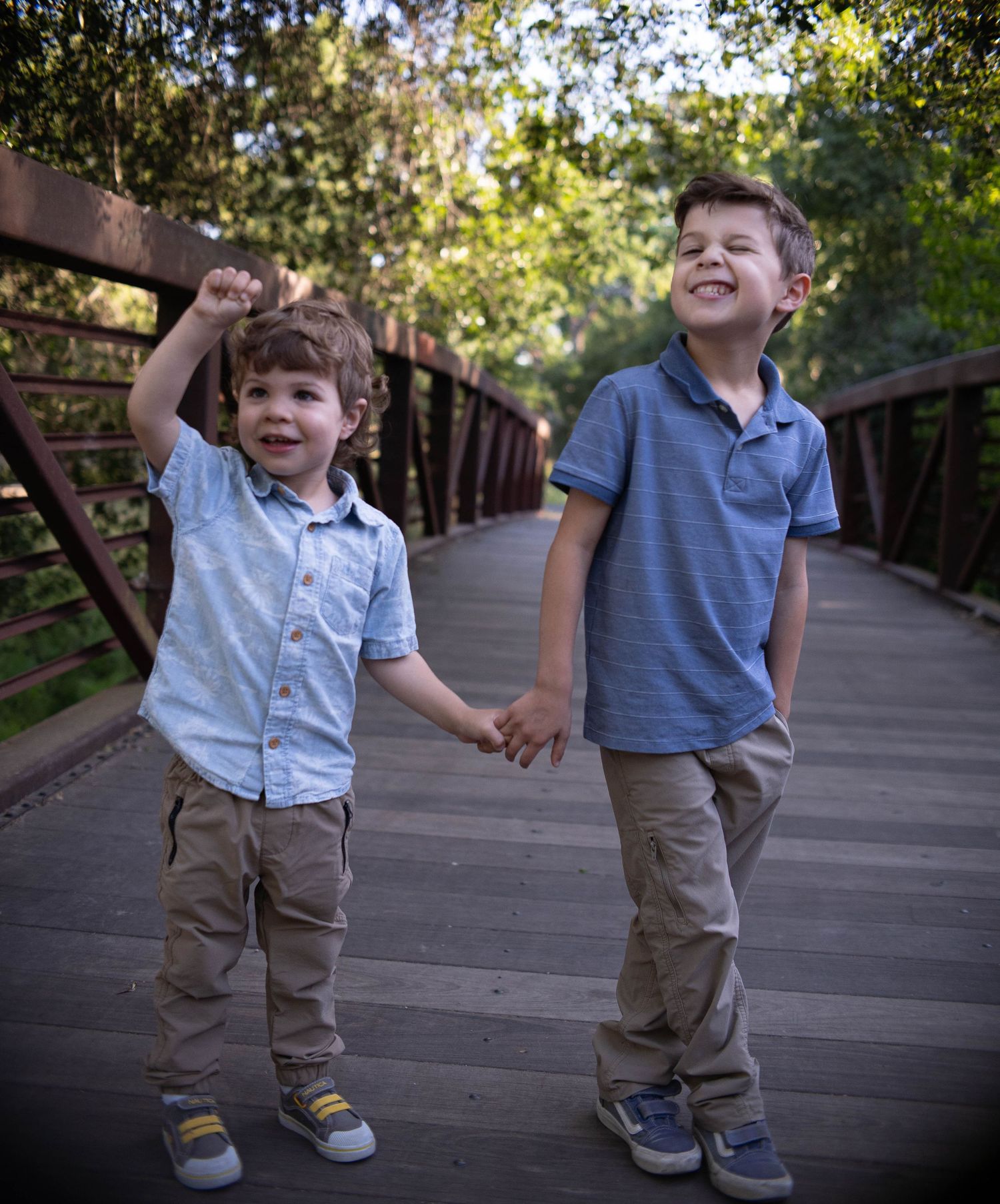 Two young children walking and playing together on a wooden boardwalk.