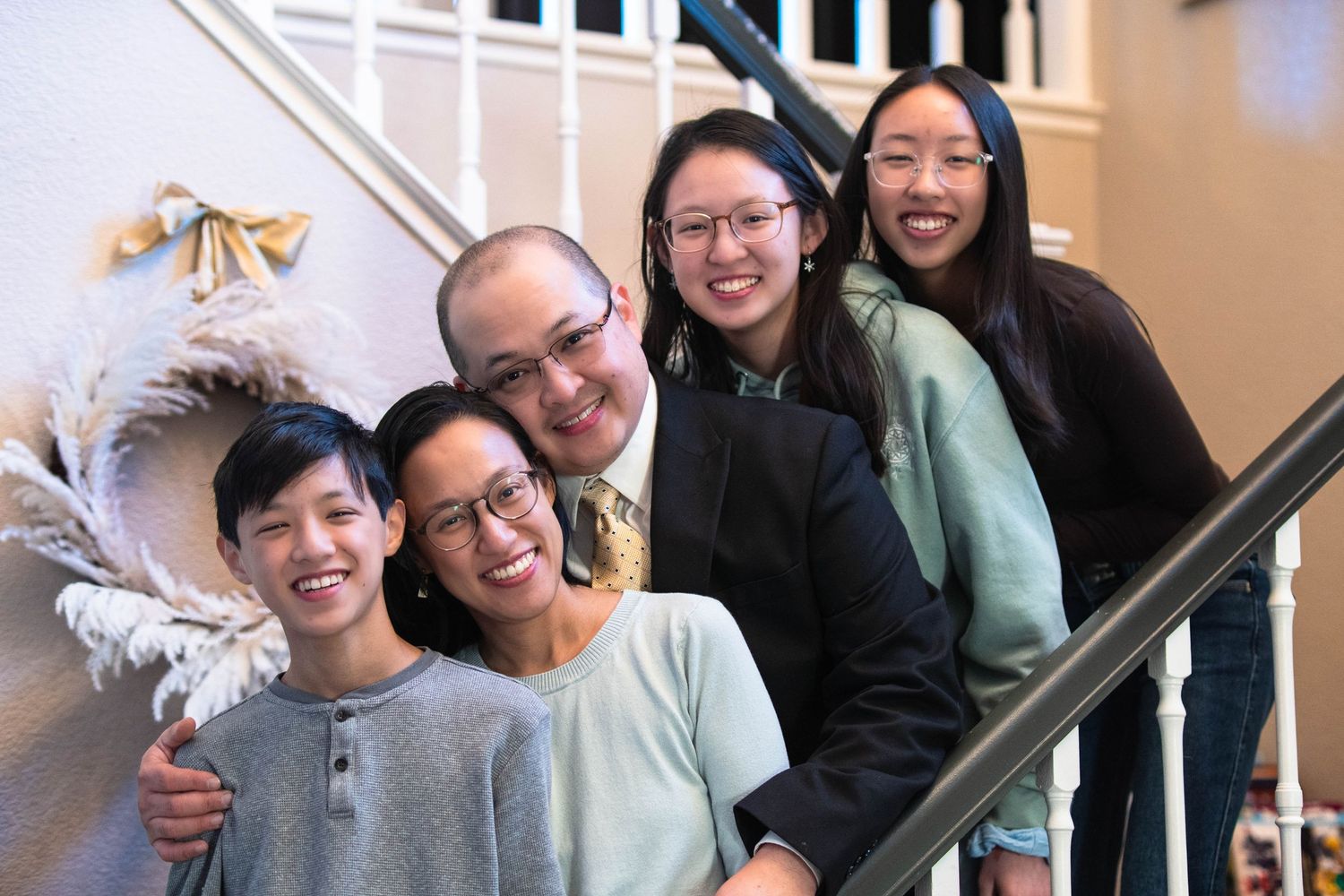 Happy Asian family of five smiling together on a staircase in a cozy home setting.