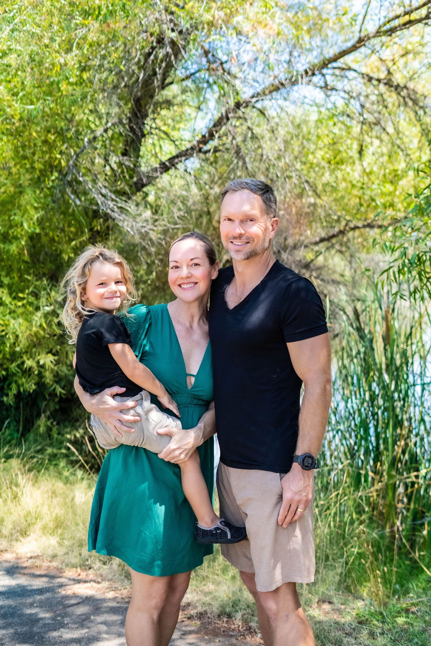 A happy family embracing outdoors on a sunny day near trees and water.