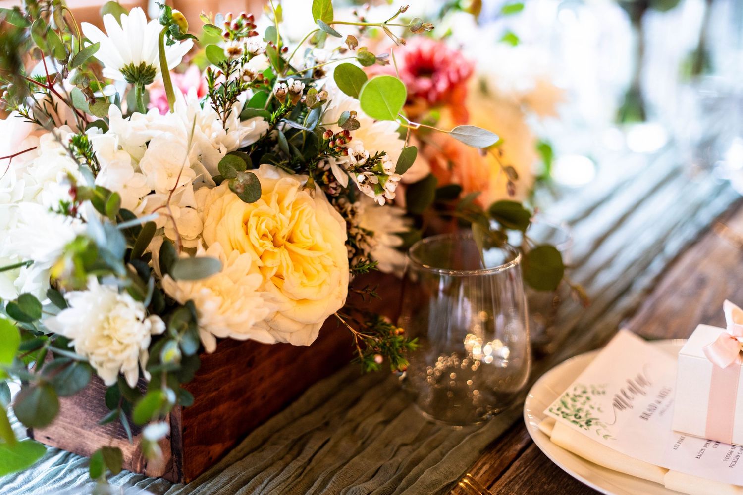 Elegant floral arrangements with peach and pink blooms decorate a rustic wedding reception table setting.