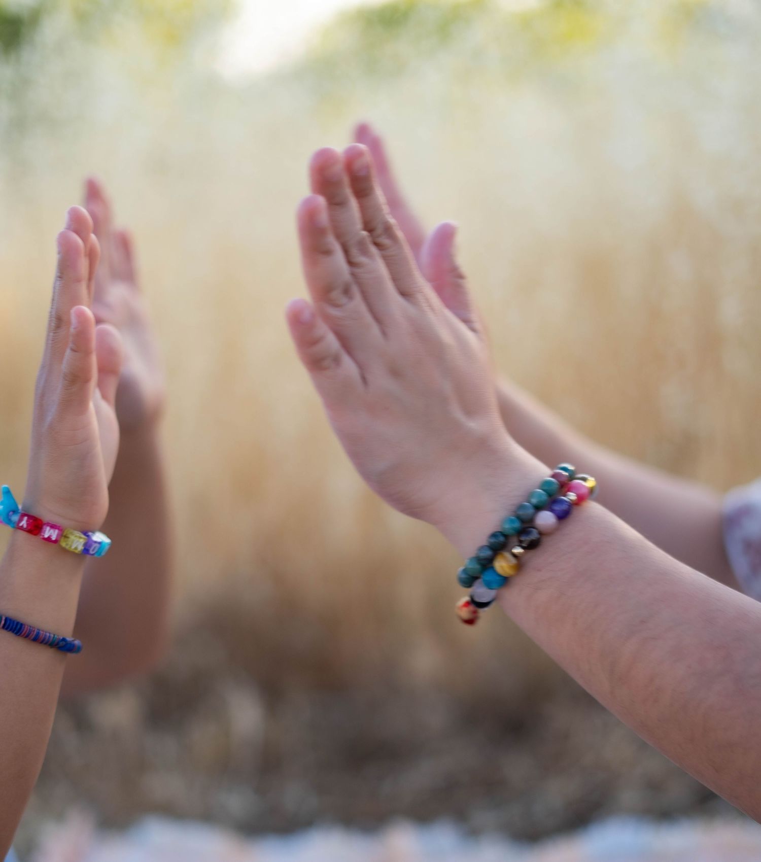 Close-up sequence of hands displaying colorful beaded bracelets against a blurred natural background.