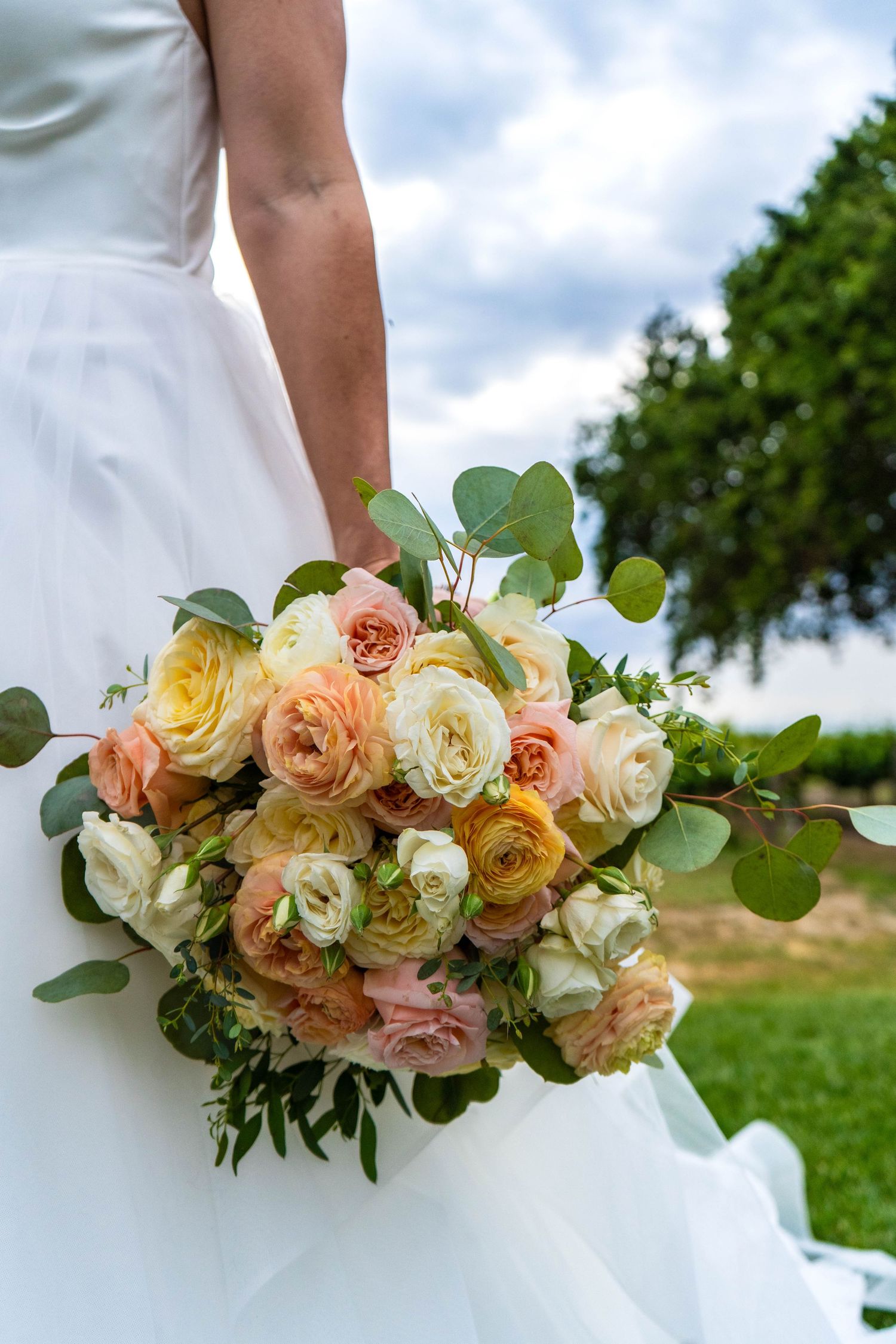 Romantic peach and cream rose bouquet with eucalyptus against white wedding dress.