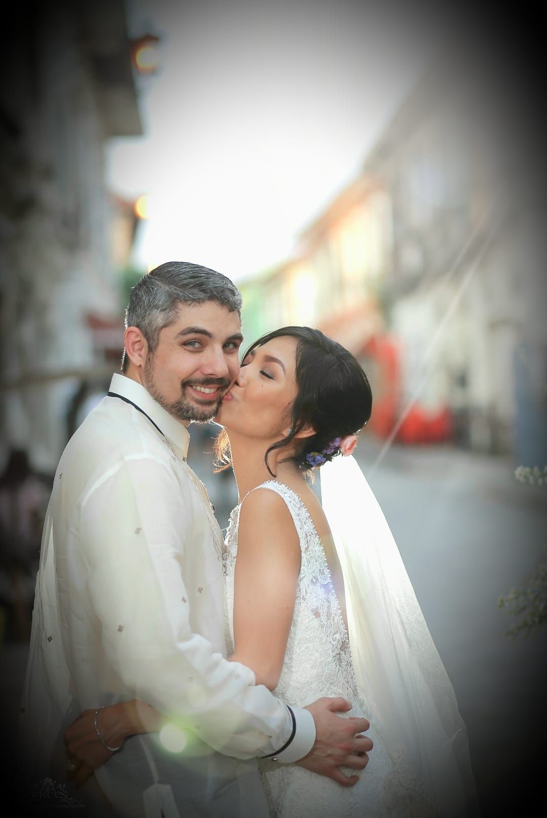 Romantic wedding couple sharing intimate moments in elegant white attire against a soft blurred background.