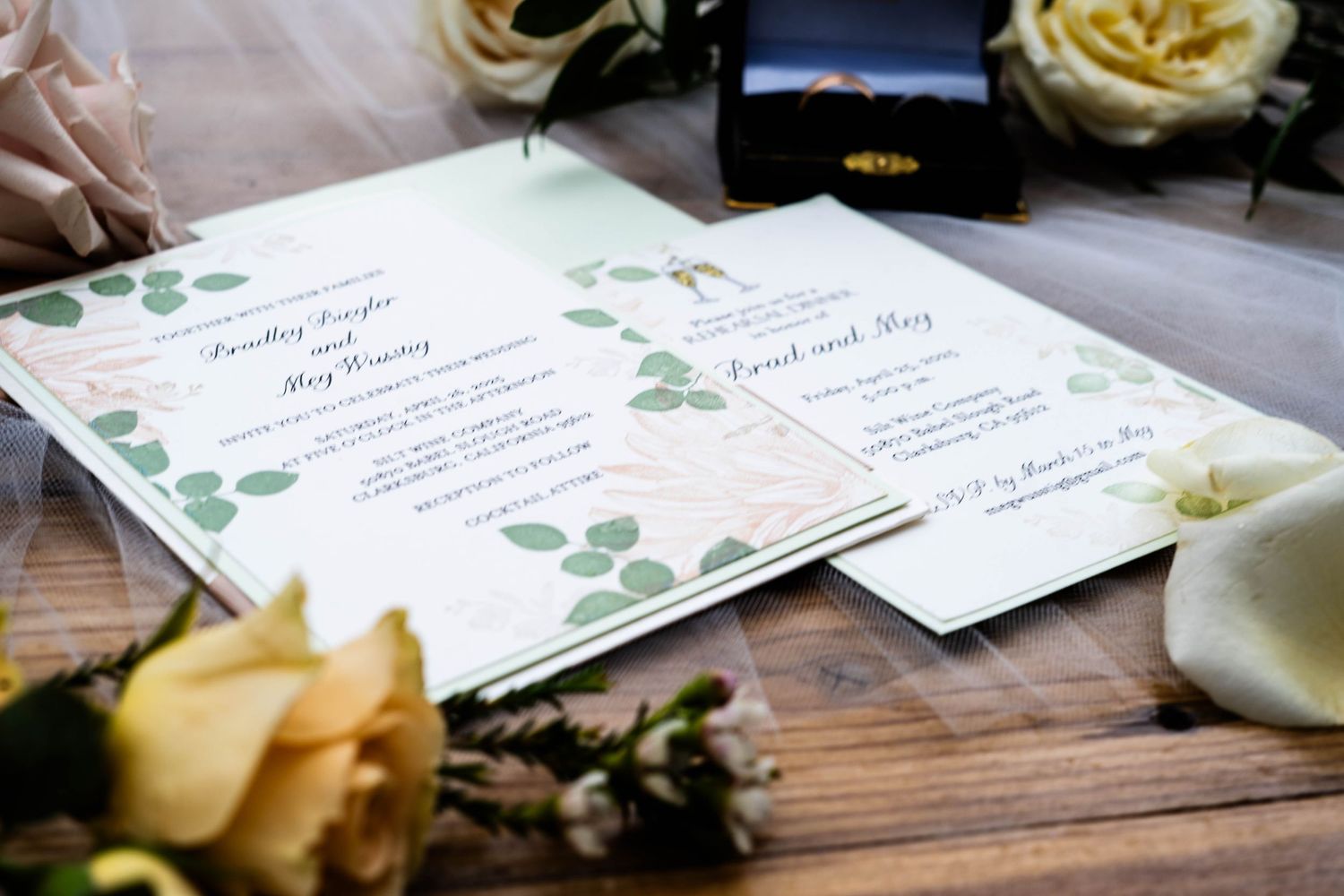 Wedding invitation suite with eucalyptus design and yellow roses on rustic wooden surface.