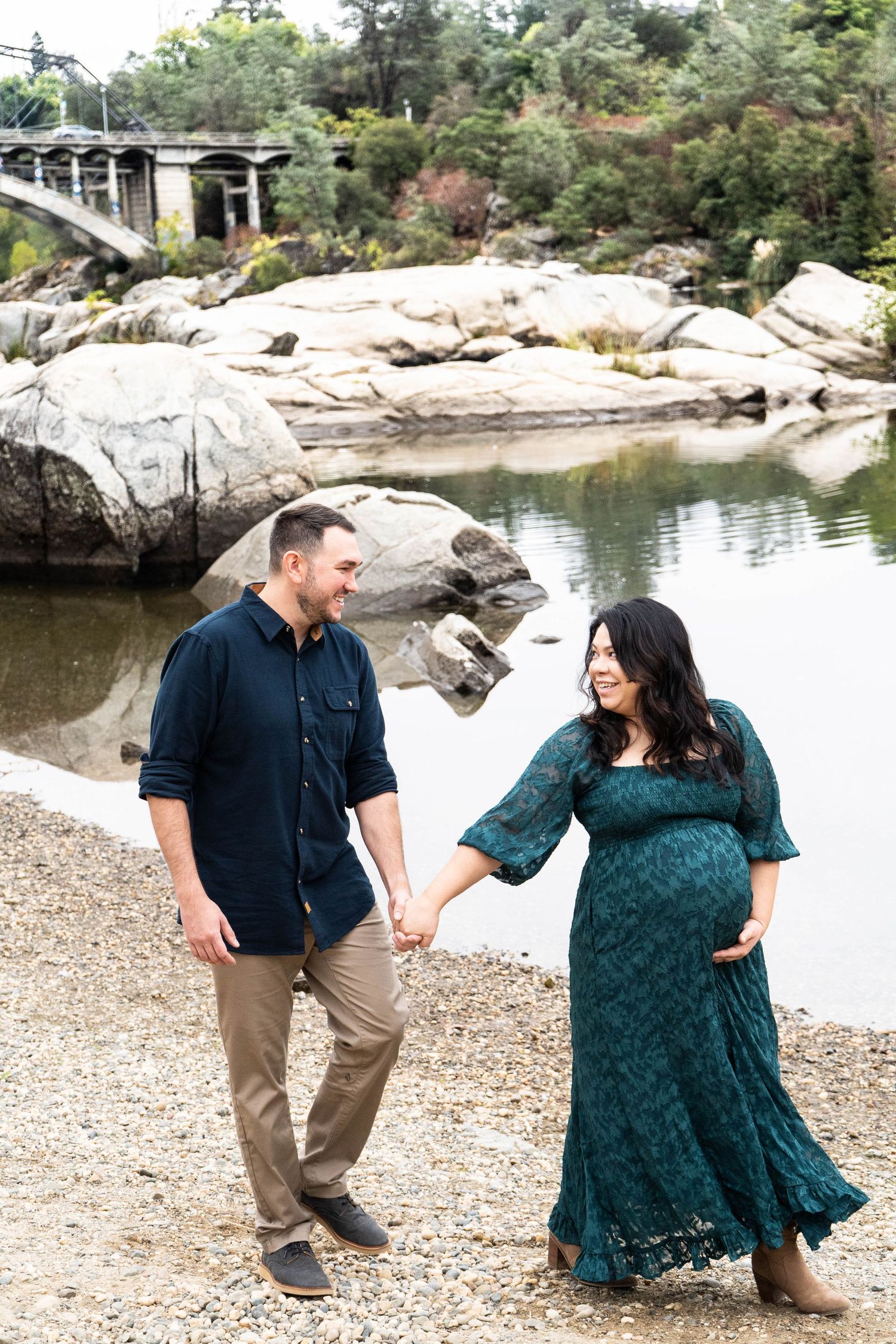 Couple in coordinating navy and teal outfits dancing and laughing together by a scenic lake.