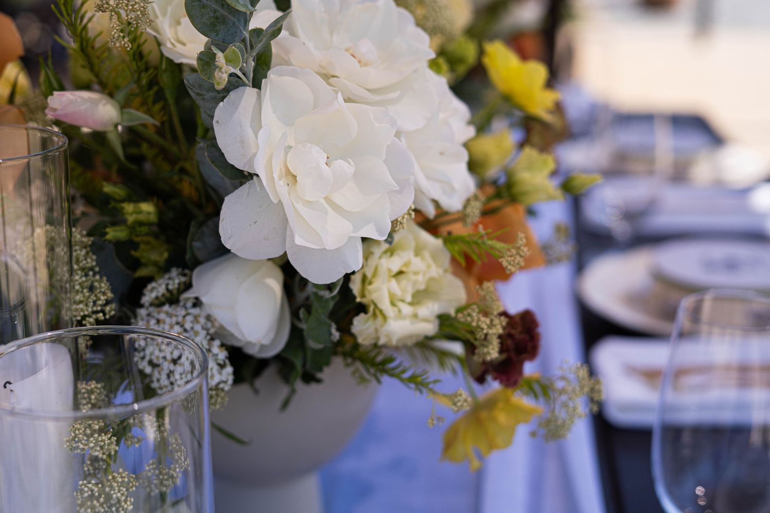 Elegant white floral centerpieces and table settings at a wedding reception.