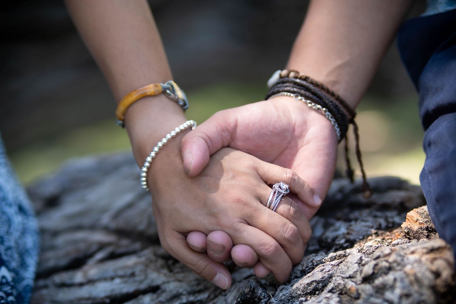 Close-up of hands holding together on textured tree bark surface.