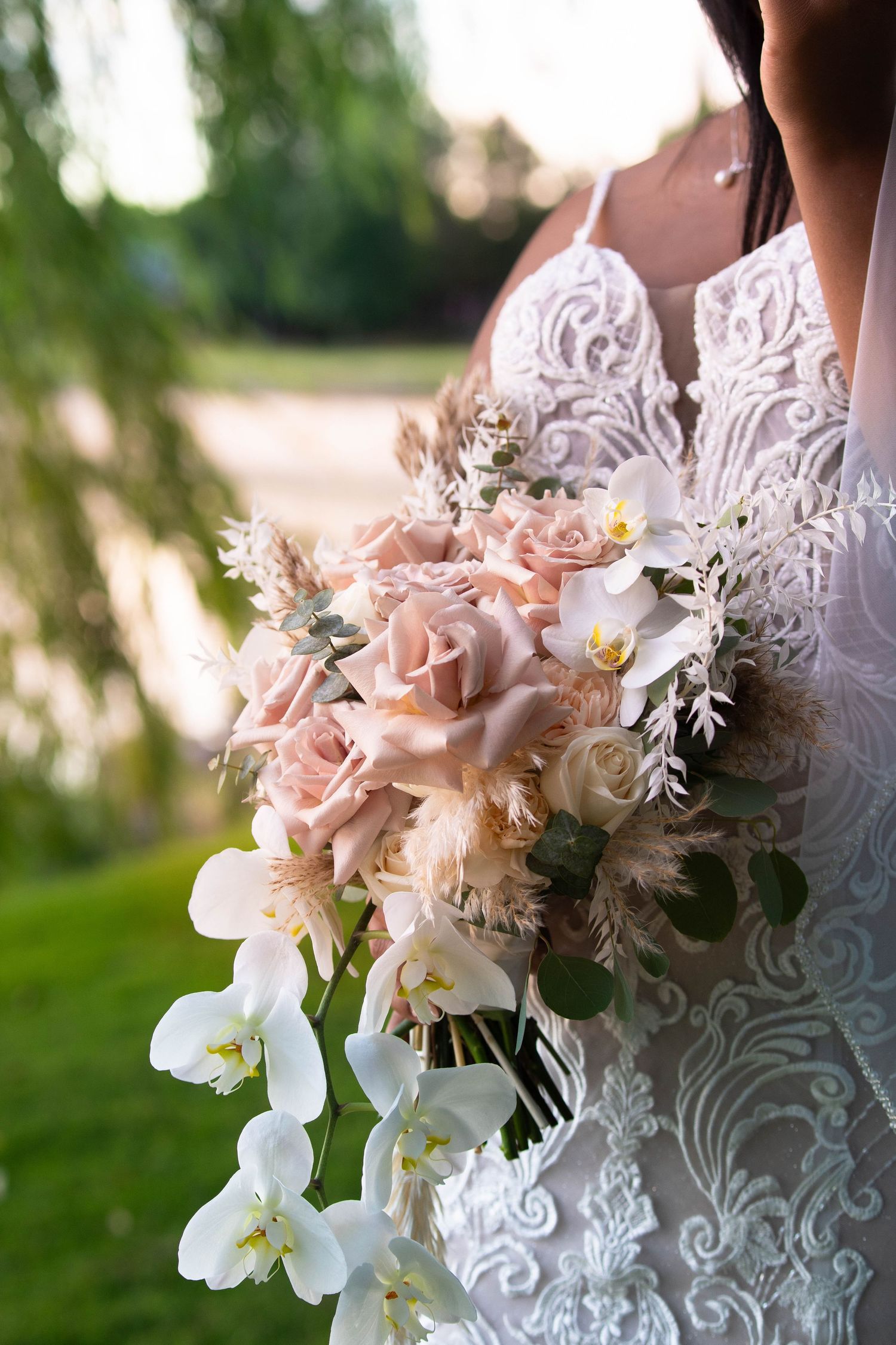 Elegant bridal bouquet featuring blush roses, white orchids and delicate greenery against a lace wedding dress.