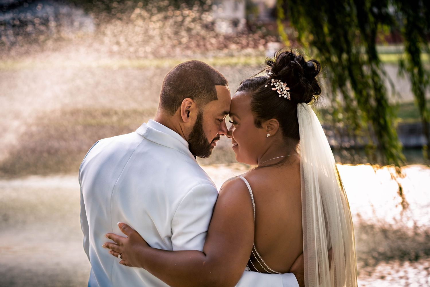 Romantic wedding couple embracing under willow trees during golden hour.