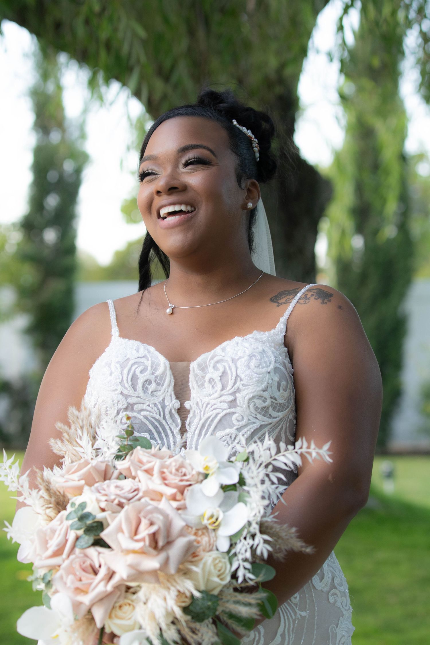 A joyful bride in a lace dress holding a blush and white bouquet.