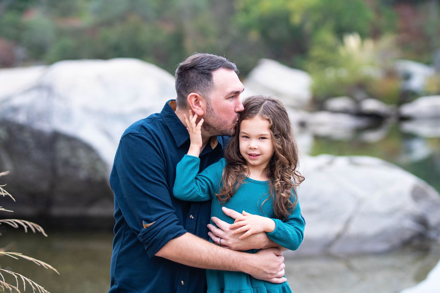 Candid family moments captured by a lake with natural rock formations in the background.