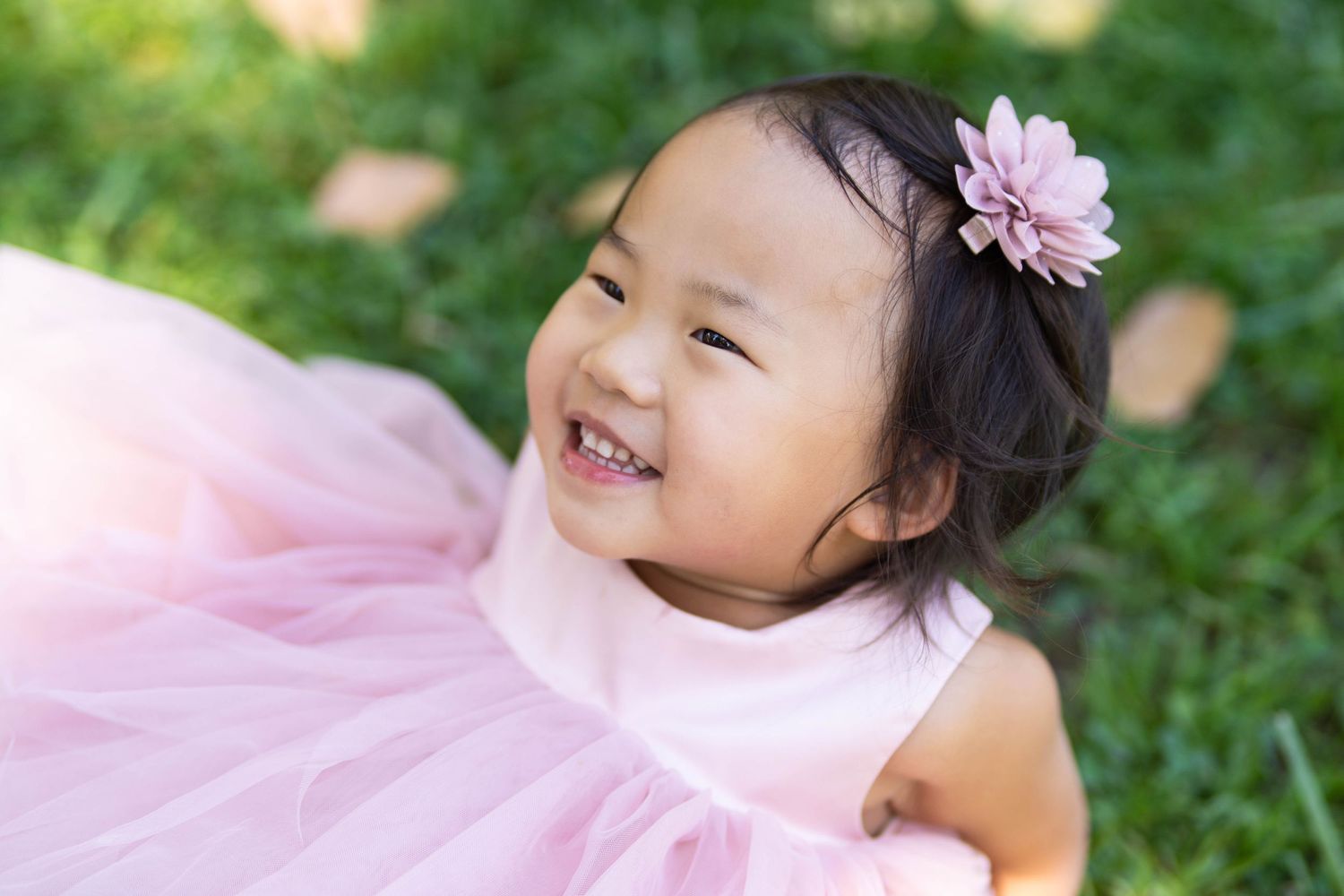 A child in a pink tutu dress smiles brightly in a garden setting.