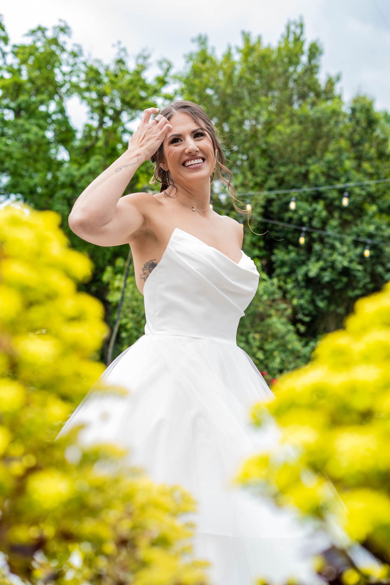 Bride in white dress against yellow flowers and green foliage on a sunny day.