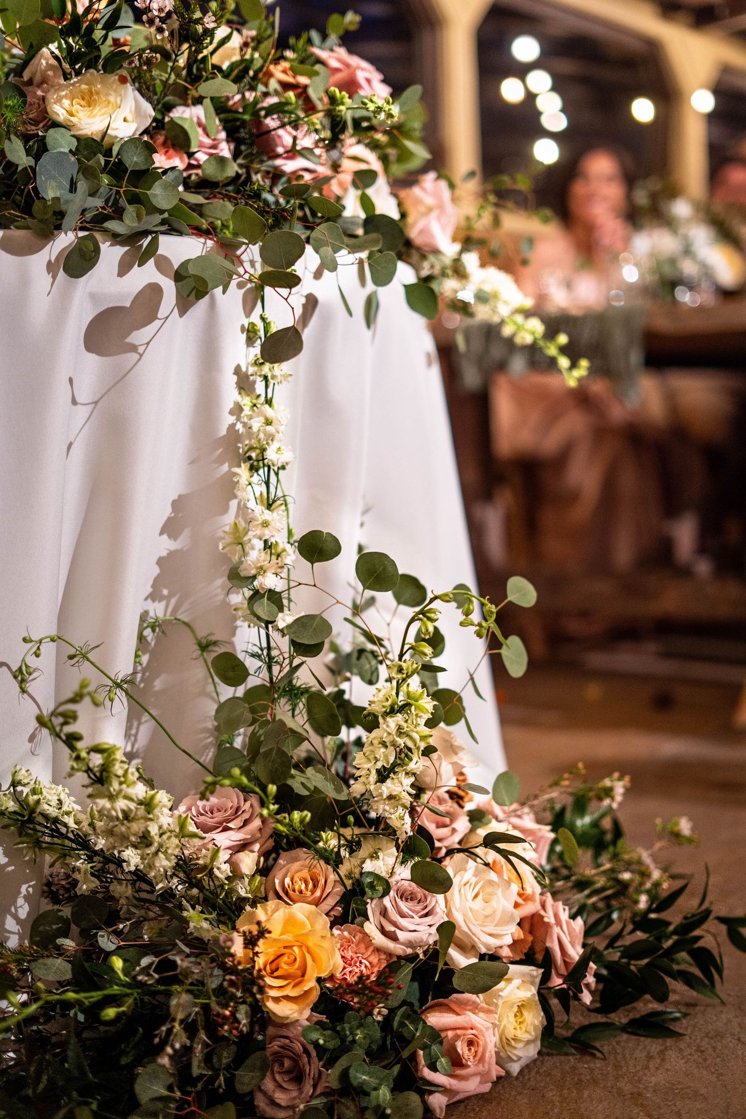 Elegant wedding floral arrangement with pink roses and eucalyptus cascading from table to floor at reception.