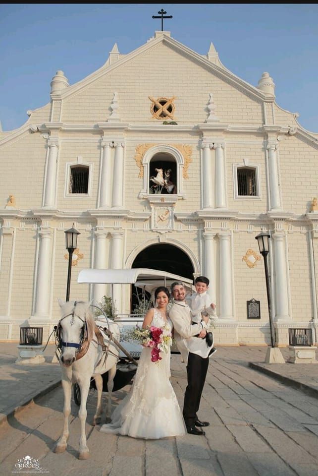 Wedding party poses playfully in front of a grand white church with classical architecture.