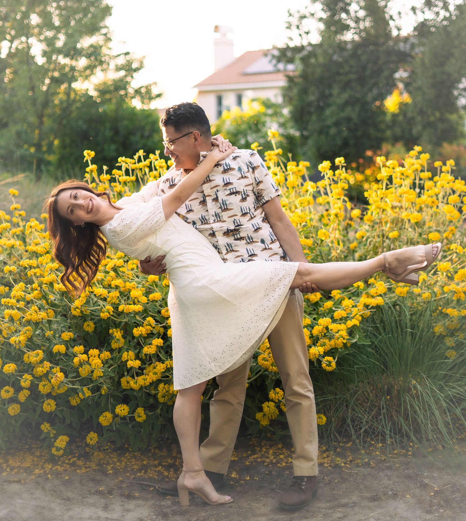 Couple dancing and posing playfully among yellow flowers in an outdoor garden setting.