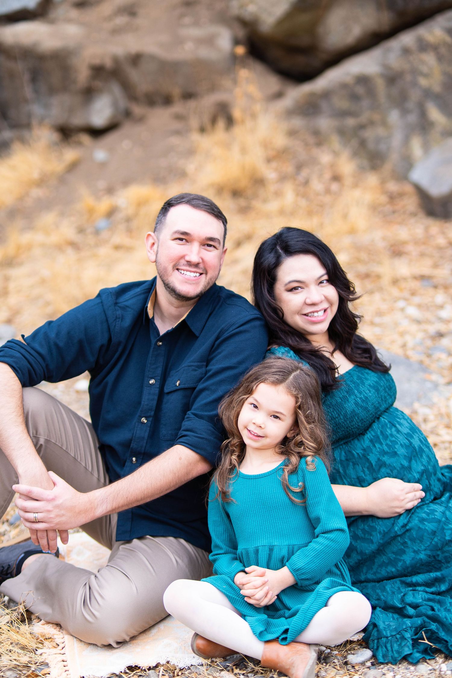 Family wearing coordinated blue and teal outfits posing together on rocks during an outdoor photo session.