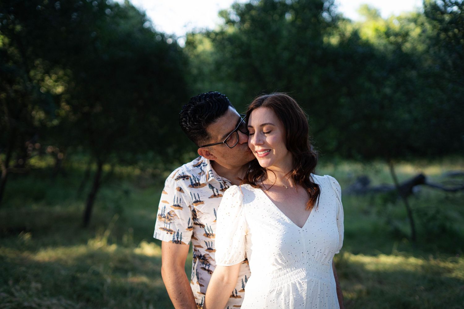 A couple sharing tender moments in a sun-dappled outdoor setting.
